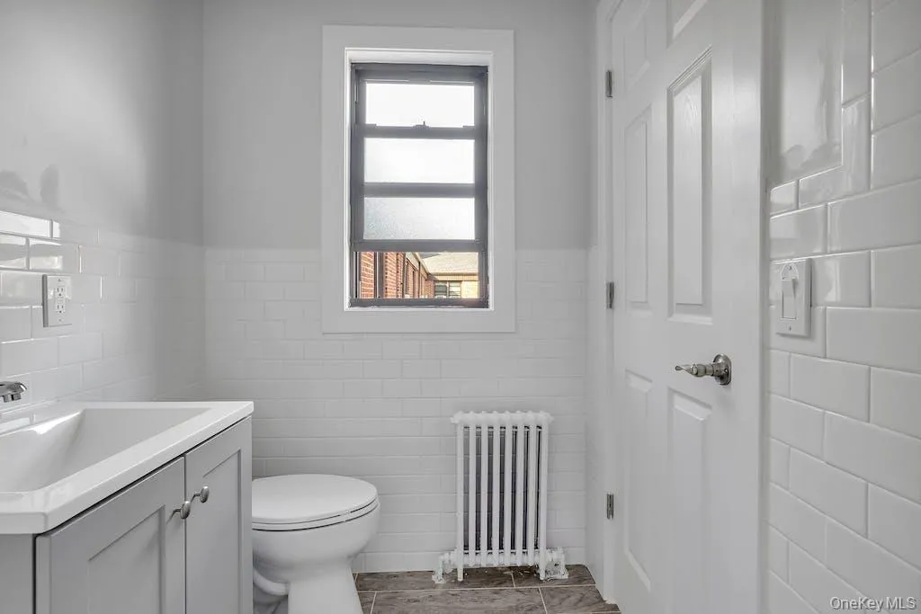 Half bathroom featuring radiator heating unit, a wainscoted wall, vanity, and tile walls Half bathroom featuring radiator heating unit, a wainscoted wall, vanity, and tile walls