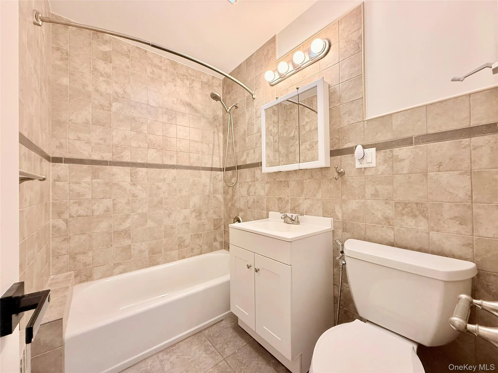 Full bath featuring vanity, shower / tub combination, tile walls, and light tile patterned floors Full bath featuring vanity, shower / tub combination, tile walls, and light tile patterned floors
