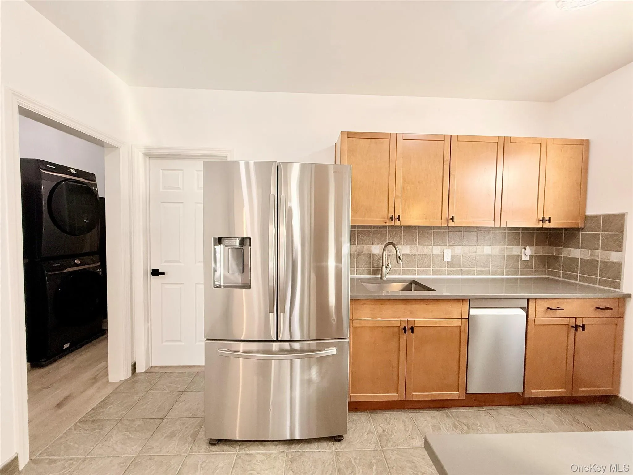 Kitchen featuring appliances with stainless steel finishes, backsplash, stacked washing machine and dryer, and light tile patterned floors Kitchen featuring appliances with stainless steel finishes, backsplash, stacked washing machine and dryer, and light tile patterned floors