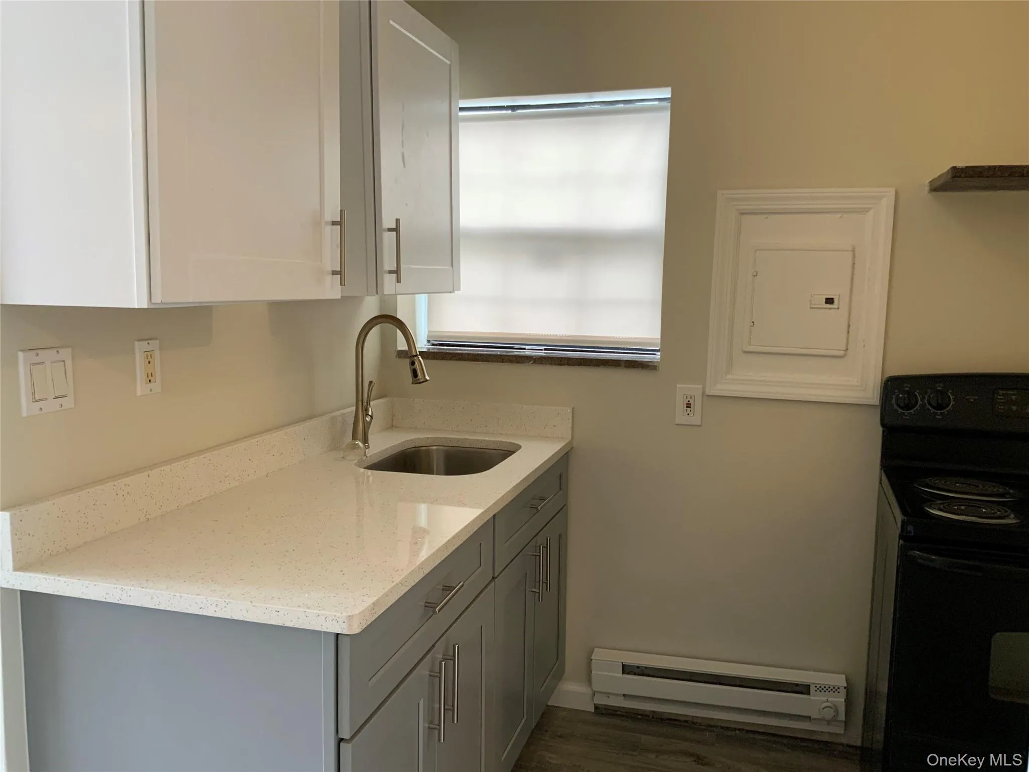 Kitchen featuring electric range, light stone countertops, baseboard heating, and white cabinetry Kitchen featuring electric range, light stone countertops, baseboard heating, and white cabinetry