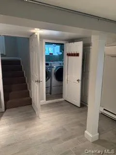 Finished below grade area with baseboard heating, washing machine and dryer, stairway, and light wood-style floors Finished below grade area with baseboard heating, washing machine and dryer, stairway, and light wood-style floors