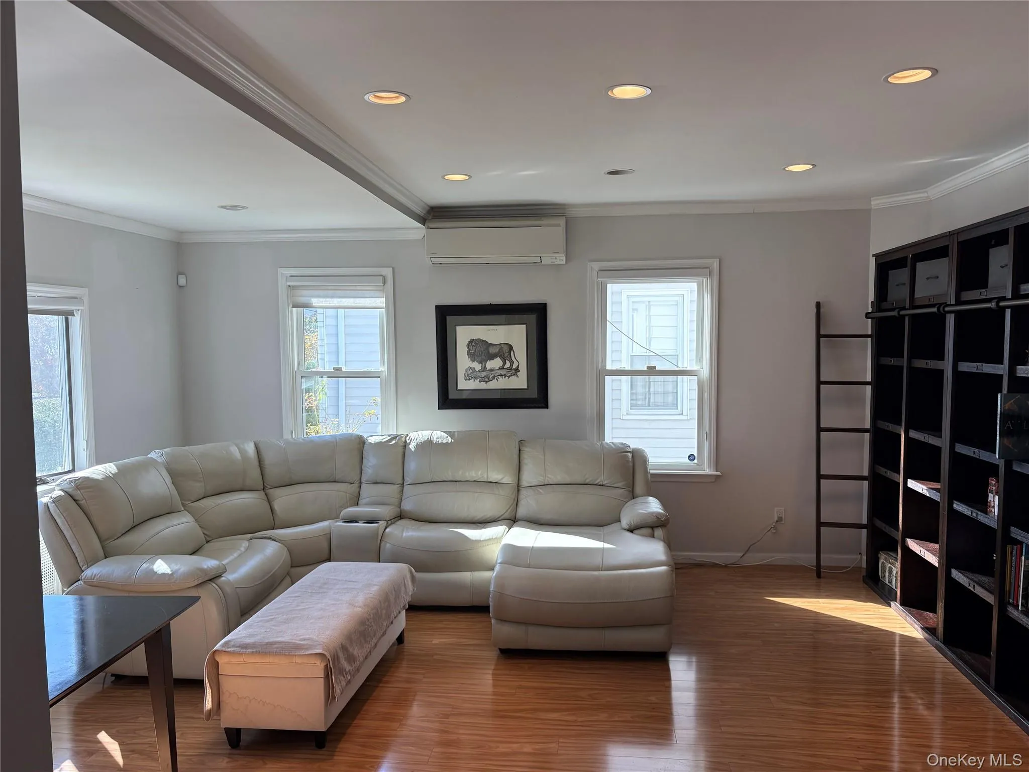 Living room with ornamental molding, wood finished floors, recessed lighting, and a wall mounted AC Living room with ornamental molding, wood finished floors, recessed lighting, and a wall mounted AC