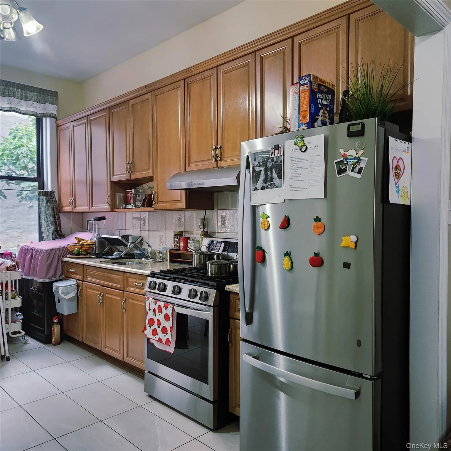 Kitchen with appliances with stainless steel finishes, brown cabinetry, light tile patterned floors, light countertops, and decorative backsplash Kitchen with appliances with stainless steel finishes, brown cabinetry, light tile patterned floors, light countertops, and decorative backsplash