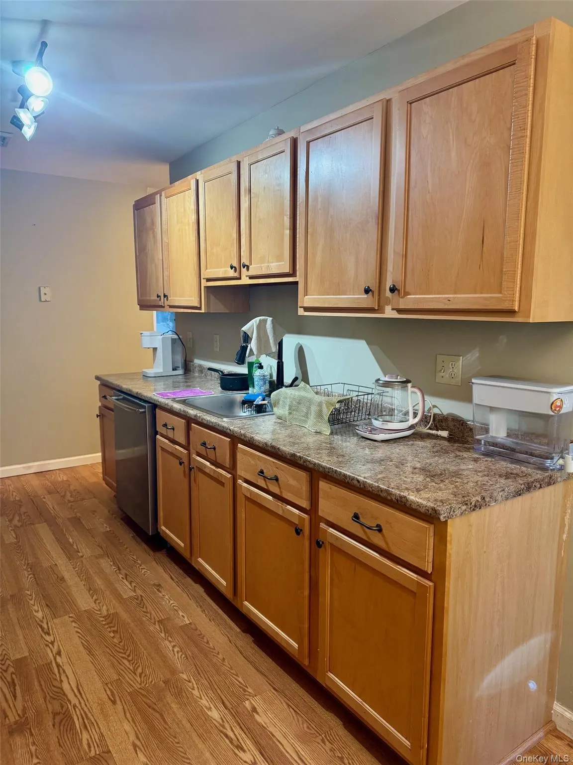 Kitchen with light wood finished floors, stainless steel dishwasher, and light countertops Kitchen with light wood finished floors, stainless steel dishwasher, and light countertops