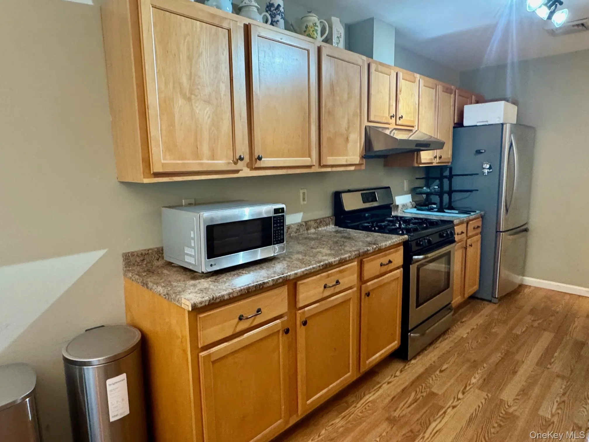 Kitchen with stainless steel appliances, under cabinet range hood, light wood-style floors, and light brown cabinetry Kitchen with stainless steel appliances, under cabinet range hood, light wood-style floors, and light brown cabinetry
