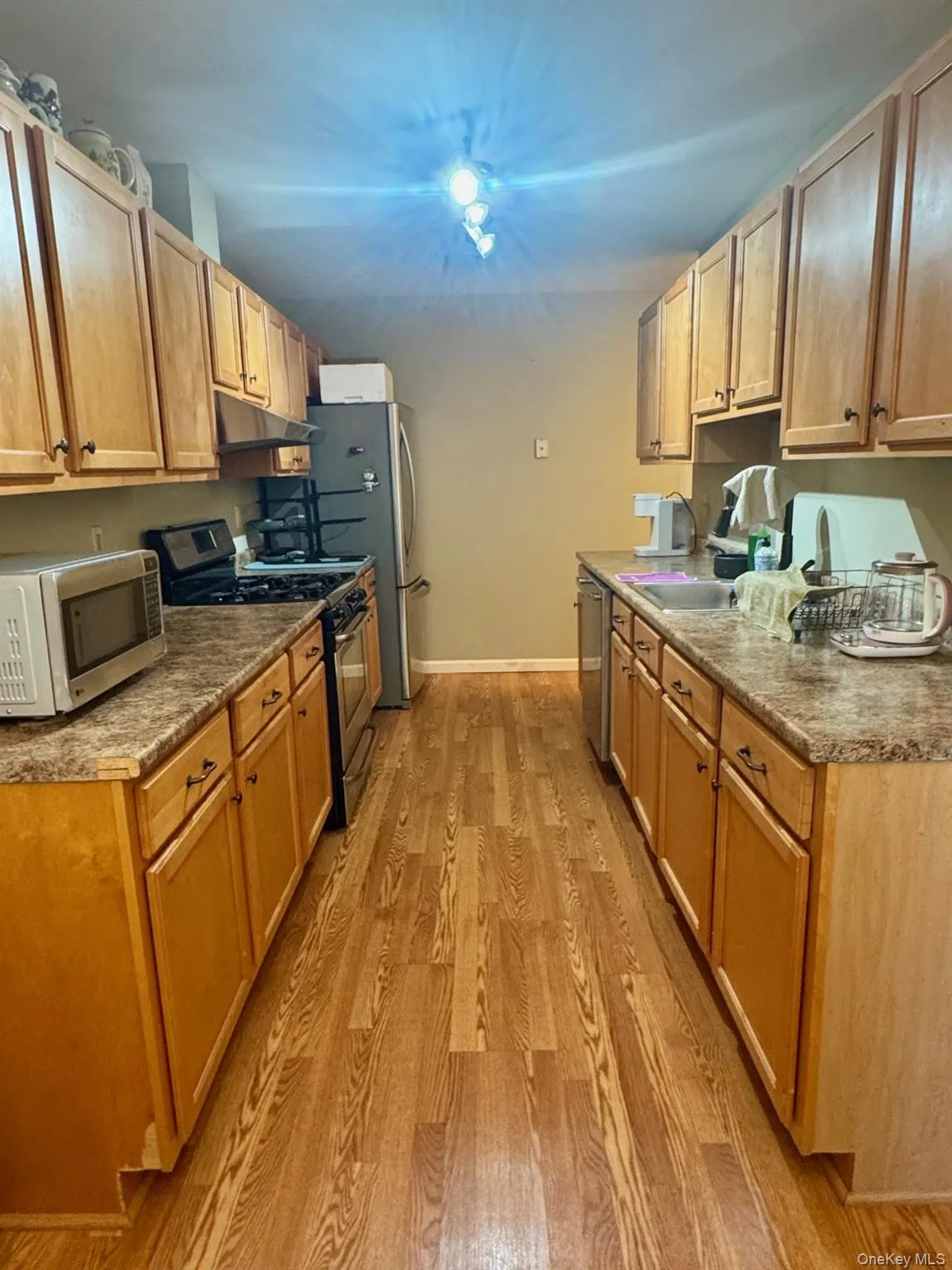 Kitchen featuring appliances with stainless steel finishes, light wood-style floors, under cabinet range hood, and brown cabinets Kitchen featuring appliances with stainless steel finishes, light wood-style floors, under cabinet range hood, and brown cabinets