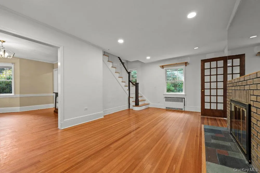 Unfurnished living room with light wood finished floors, recessed lighting, stairway, radiator, and a brick fireplace Unfurnished living room with light wood finished floors, recessed lighting, stairway, radiator, and a brick fireplace