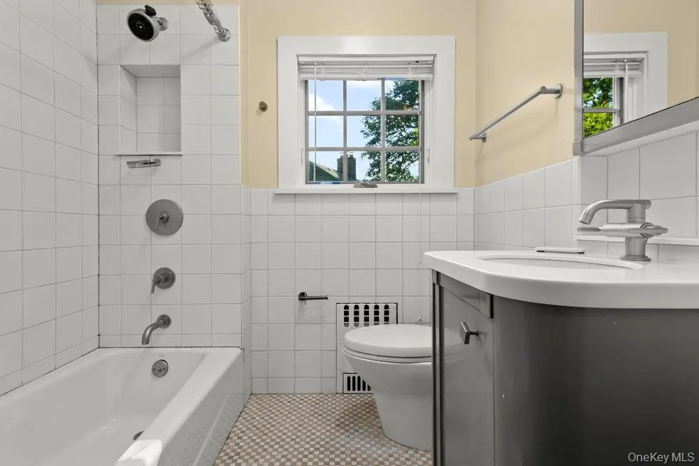 Full bathroom with tile walls, radiator heating unit, vanity, washtub / shower combination, and tile patterned flooring Full bathroom with tile walls, radiator heating unit, vanity, washtub / shower combination, and tile patterned flooring