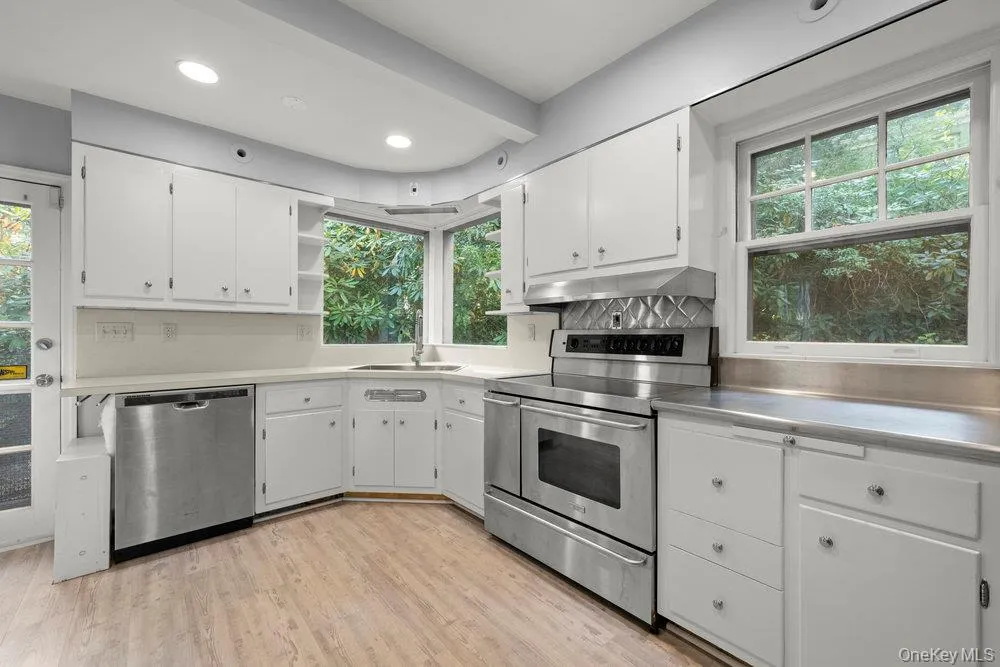 Kitchen featuring appliances with stainless steel finishes, white cabinetry, stainless steel countertops, open shelves, and light wood-style floors Kitchen featuring appliances with stainless steel finishes, white cabinetry, stainless steel countertops, open shelves, and light wood-style floors