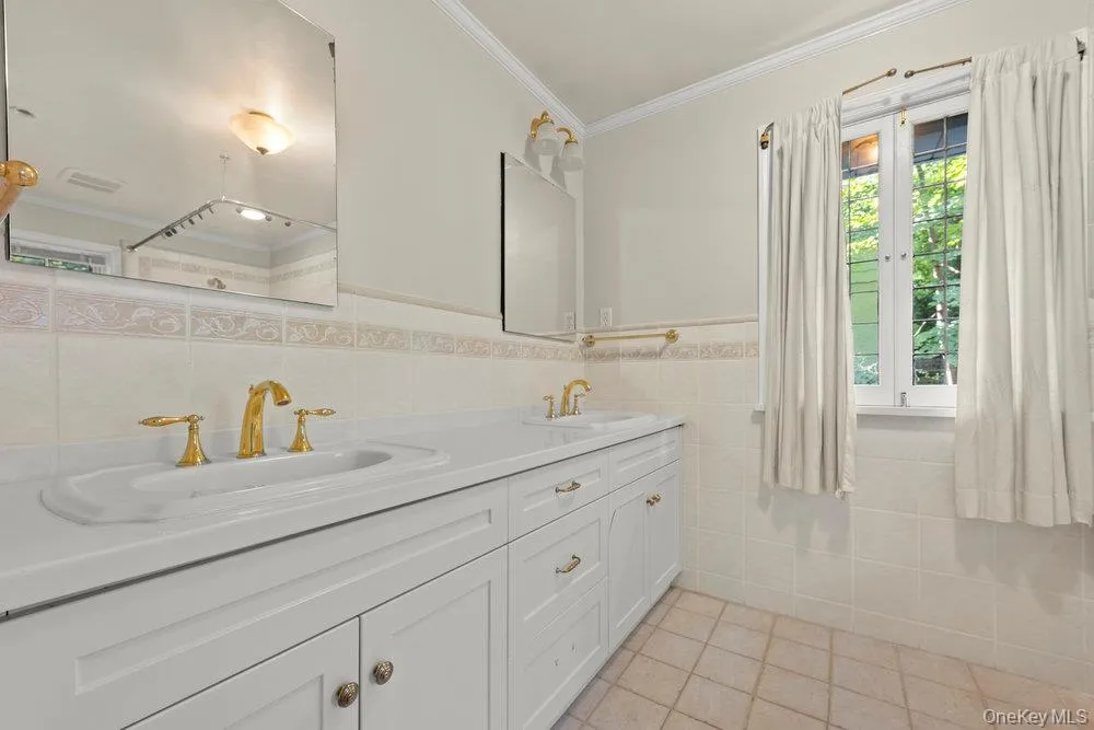 Full bath with light tile patterned floors, tile walls, ornamental molding, and double vanity Full bath with light tile patterned floors, tile walls, ornamental molding, and double vanity