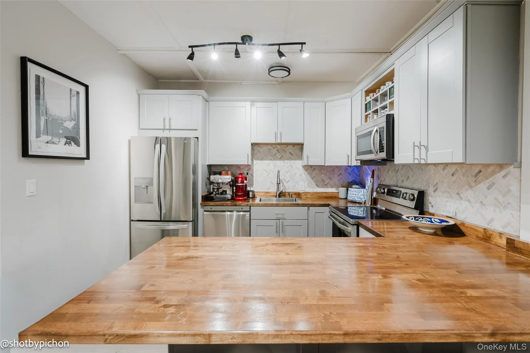Kitchen with tasteful backsplash, appliances with stainless steel finishes, wood counters, white cabinetry, and track lighting Kitchen with tasteful backsplash, appliances with stainless steel finishes, wood counters, white cabinetry, and track lighting