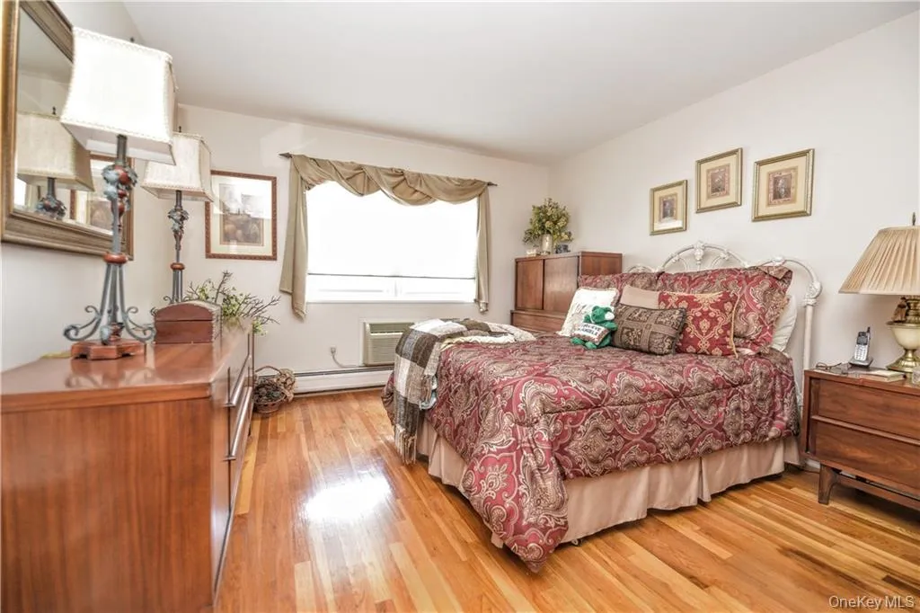 Bedroom featuring light wood-style floors, a baseboard heating unit, and a wall unit AC Bedroom featuring light wood-style floors, a baseboard heating unit, and a wall unit AC