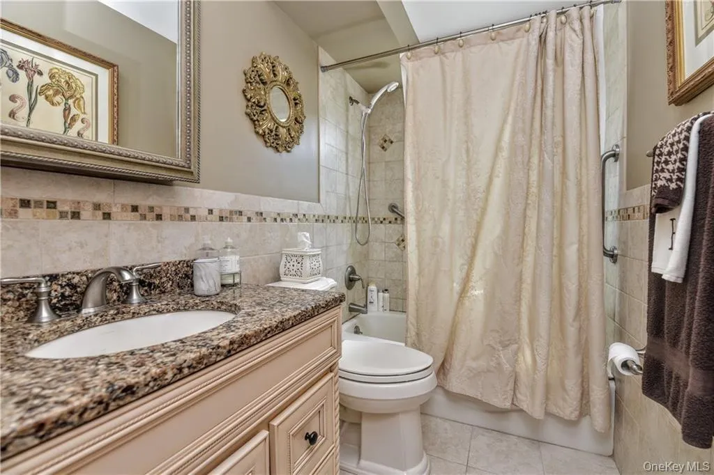 Bathroom with tile walls, shower / bath combo with shower curtain, vanity, and light tile patterned flooring Bathroom with tile walls, shower / bath combo with shower curtain, vanity, and light tile patterned flooring