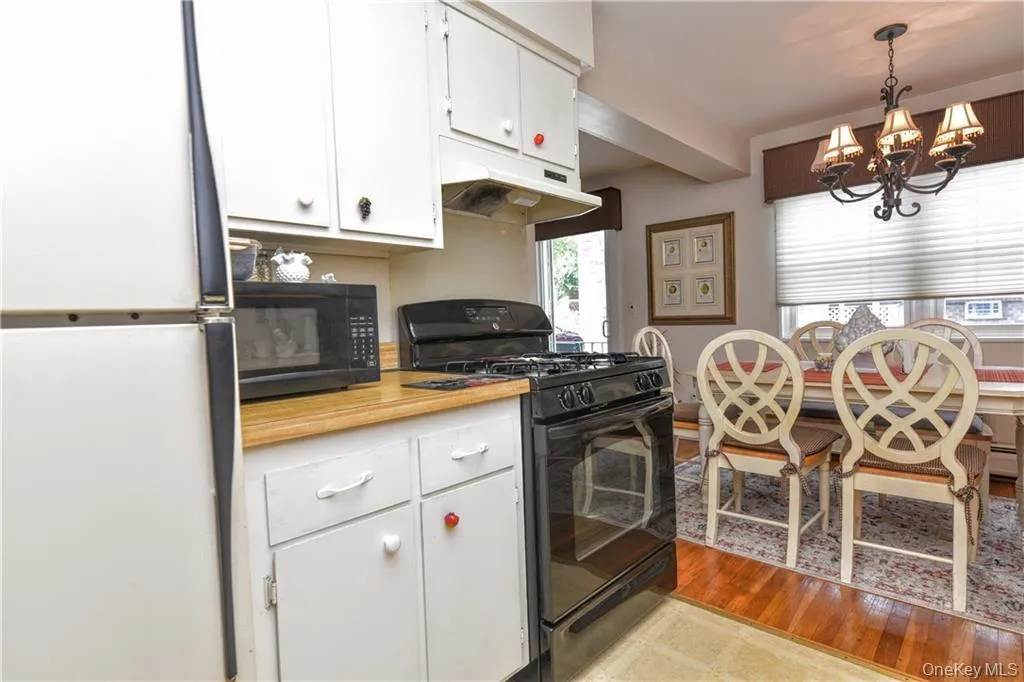 Kitchen featuring black appliances, white cabinets, light countertops, light wood-type flooring, and under cabinet range hood Kitchen featuring black appliances, white cabinets, light countertops, light wood-type flooring, and under cabinet range hood