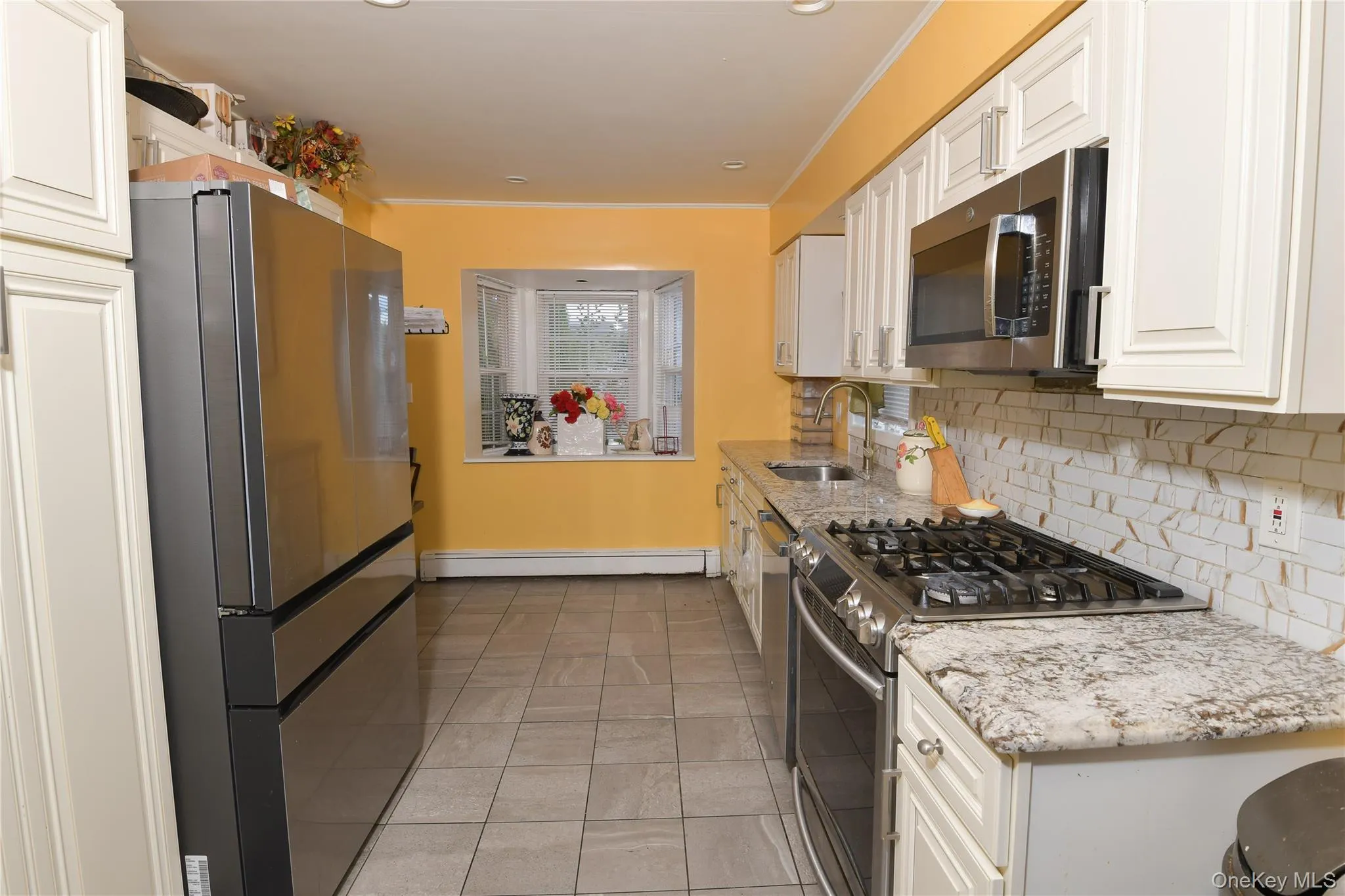 Kitchen featuring stainless steel appliances, light tile patterned flooring, decorative backsplash, light stone countertops, and white cabinetry Kitchen featuring stainless steel appliances, light tile patterned flooring, decorative backsplash, light stone countertops, and white cabinetry