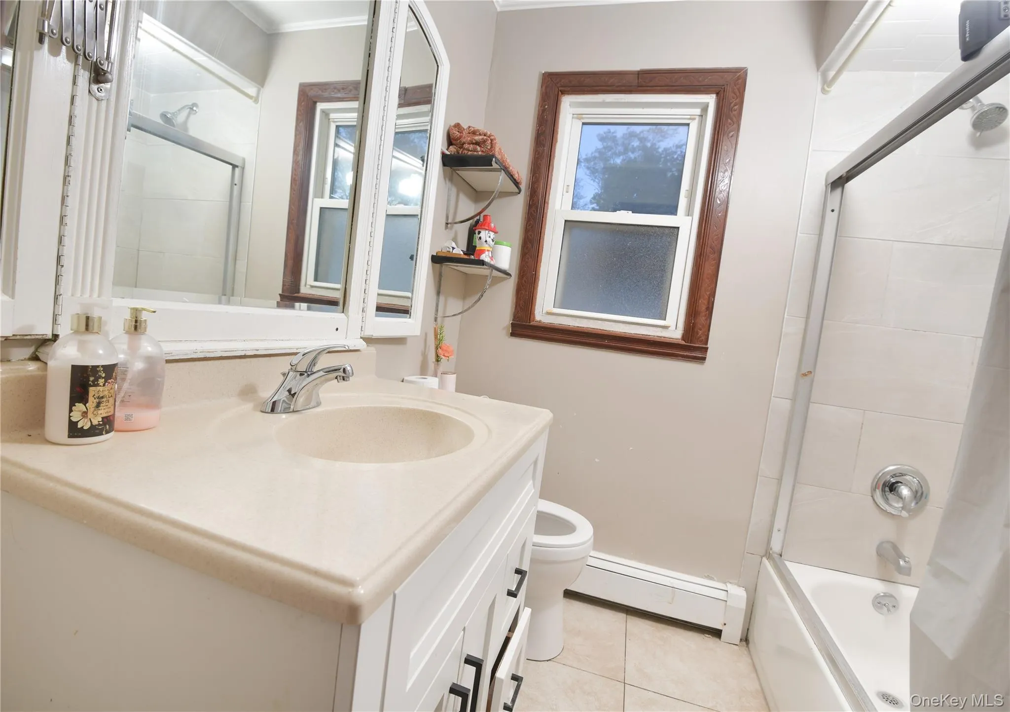 Full bathroom featuring vanity, a baseboard radiator, light tile patterned floors, and combined bath / shower with glass door Full bathroom featuring vanity, a baseboard radiator, light tile patterned floors, and combined bath / shower with glass door