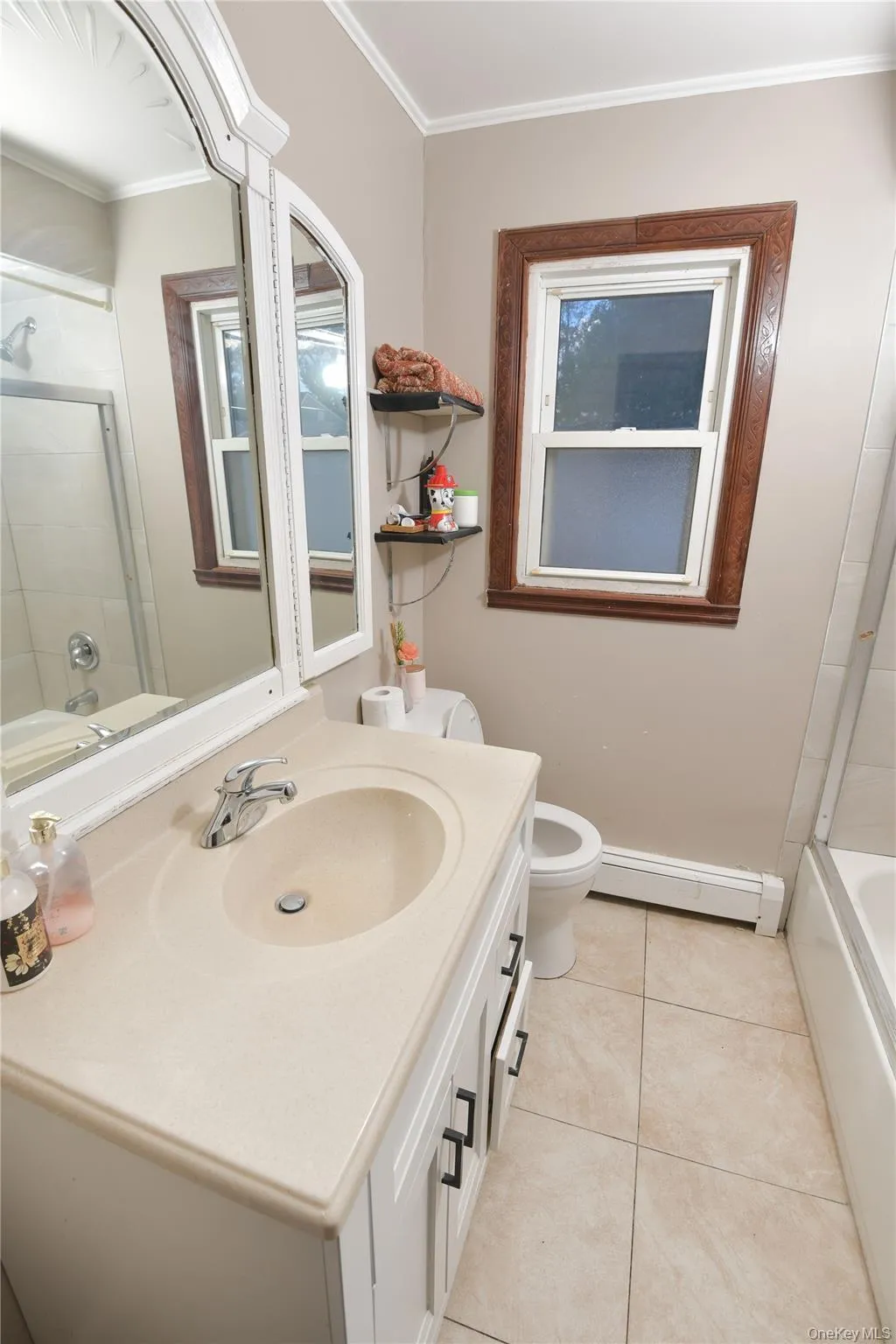 Bathroom with shower / bath combination with glass door, vanity, crown molding, baseboard heating, and light tile patterned floors Bathroom with shower / bath combination with glass door, vanity, crown molding, baseboard heating, and light tile patterned floors