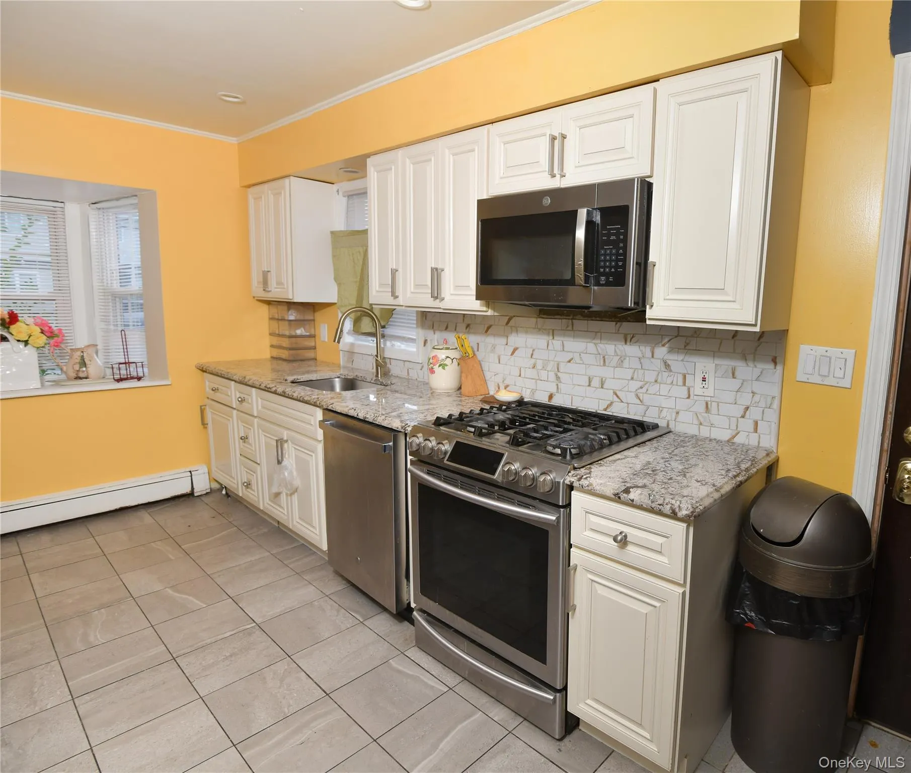 Kitchen featuring appliances with stainless steel finishes, backsplash, light stone countertops, light tile patterned floors, and ornamental molding Kitchen featuring appliances with stainless steel finishes, backsplash, light stone countertops, light tile patterned floors, and ornamental molding