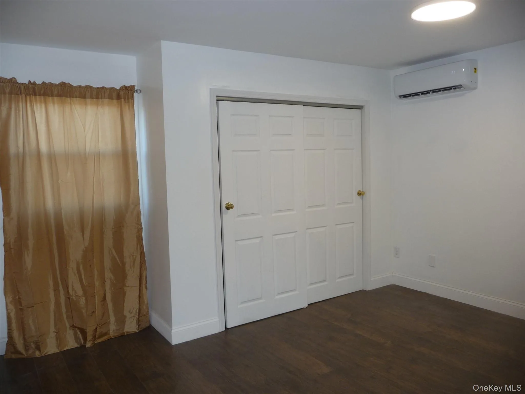 Unfurnished bedroom featuring dark wood-type flooring, a closet, and a wall unit AC Unfurnished bedroom featuring dark wood-type flooring, a closet, and a wall unit AC