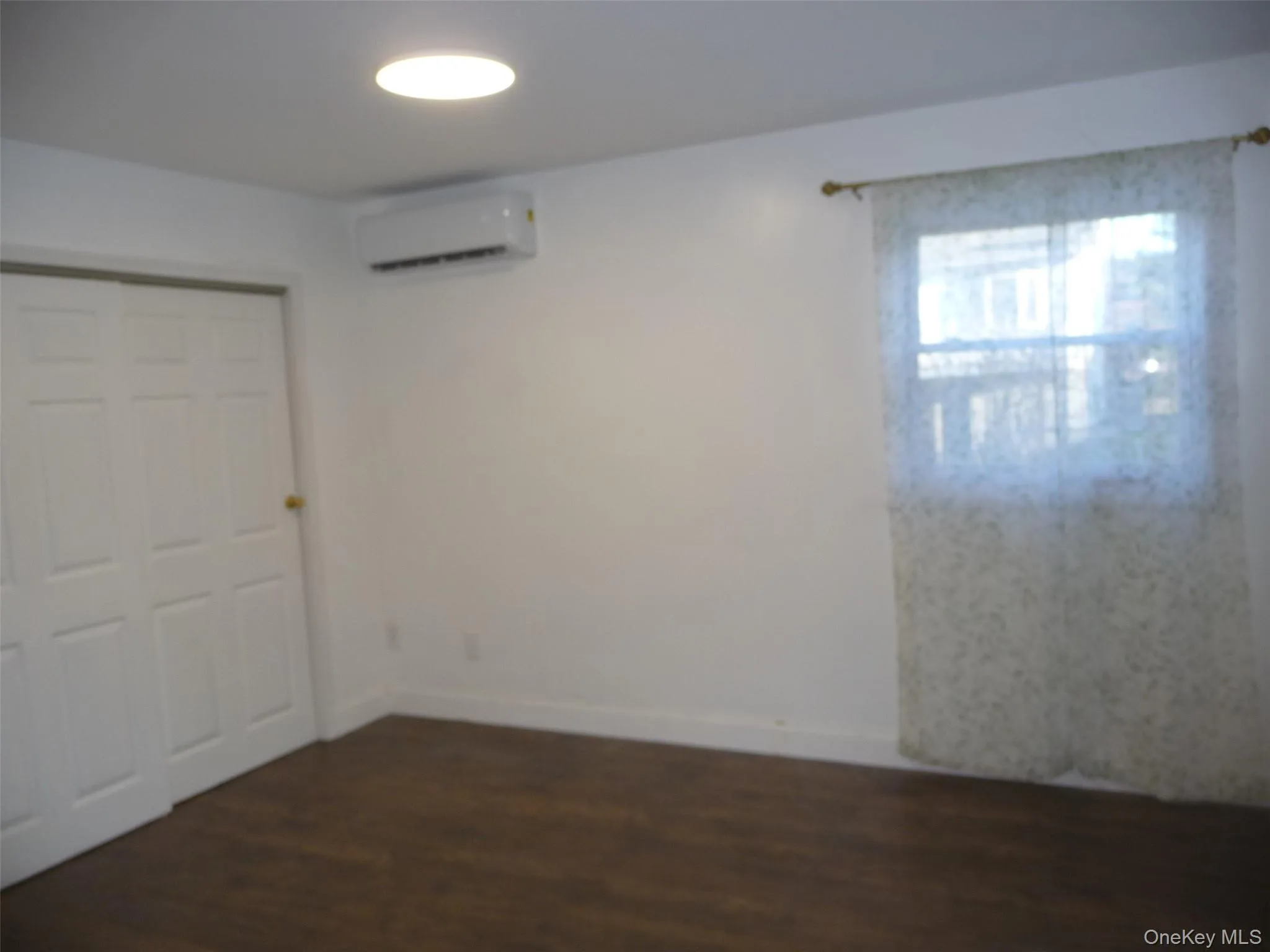 Unfurnished bedroom featuring a closet, dark wood finished floors, and a wall unit AC Unfurnished bedroom featuring a closet, dark wood finished floors, and a wall unit AC