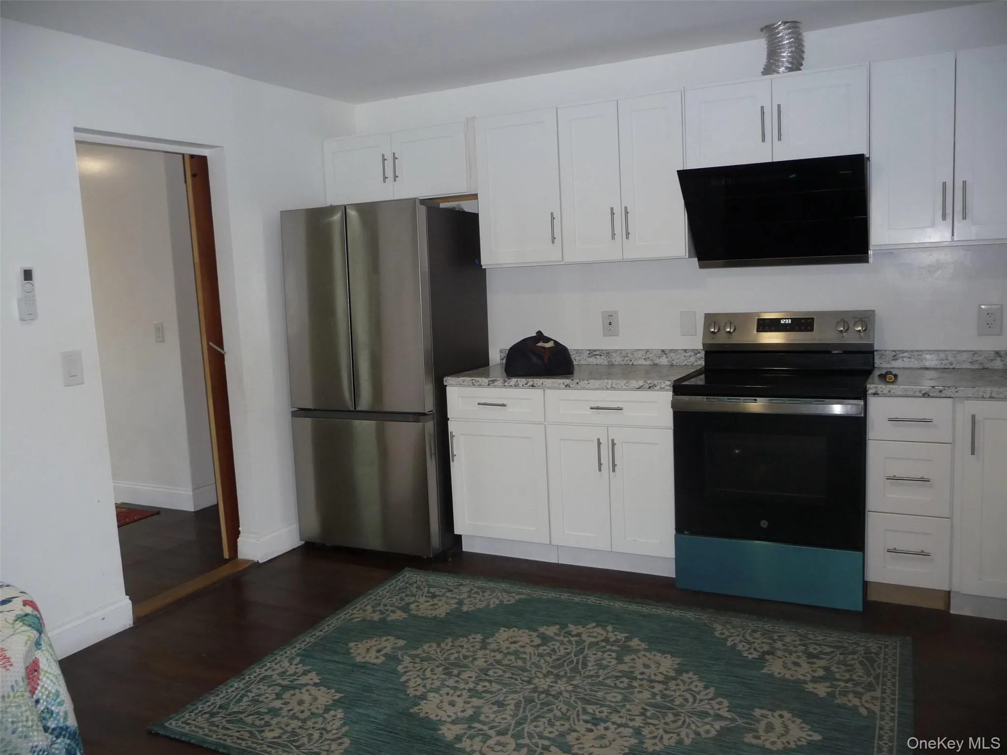 Kitchen with stainless steel appliances, white cabinets, dark wood-style floors, and light stone countertops Kitchen with stainless steel appliances, white cabinets, dark wood-style floors, and light stone countertops