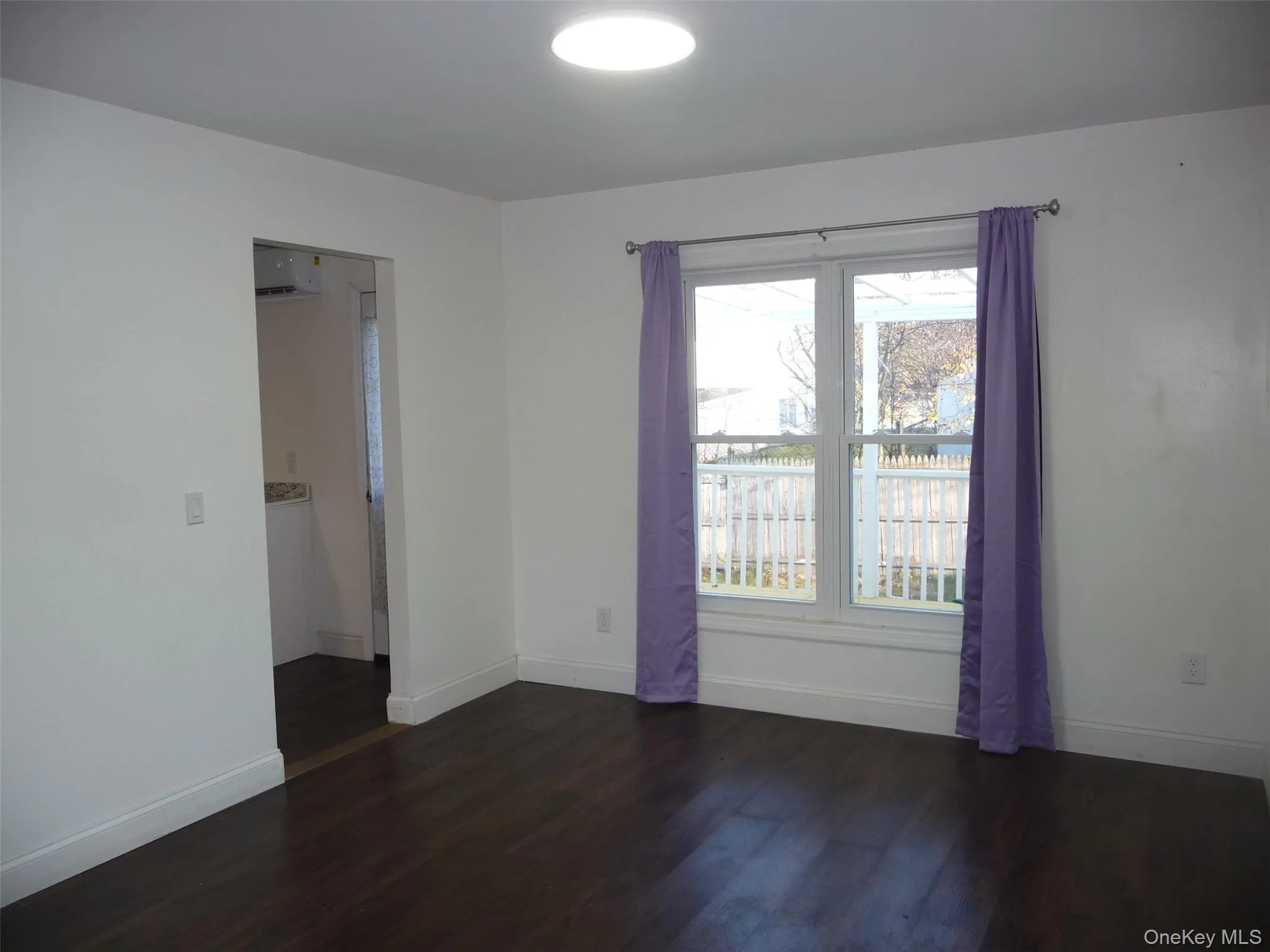 Empty room with dark wood finished floors, a wall mounted AC, and a water view Empty room with dark wood finished floors, a wall mounted AC, and a water view
