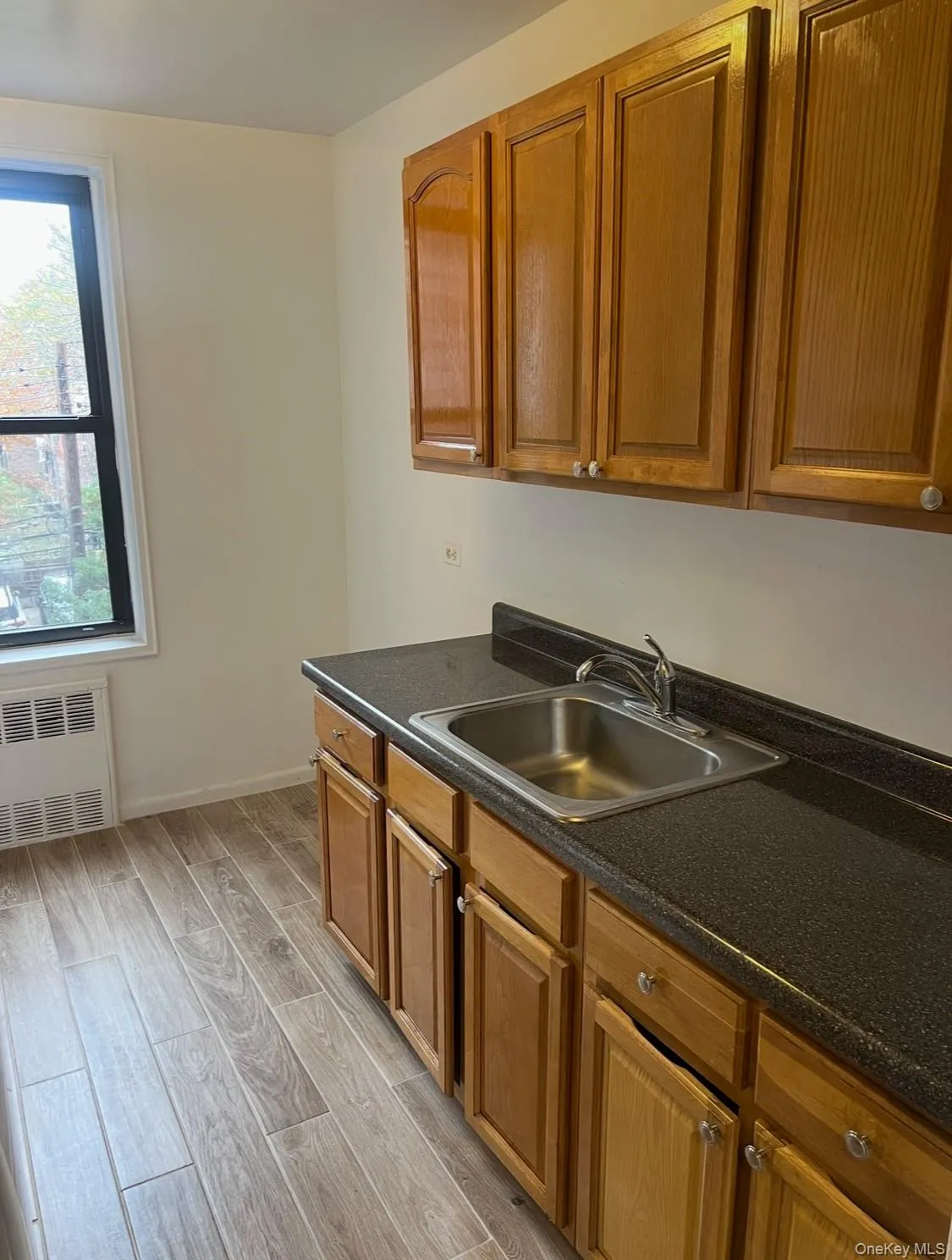Kitchen featuring dark countertops, light wood-style flooring, radiator heating unit, and brown cabinets Kitchen featuring dark countertops, light wood-style flooring, radiator heating unit, and brown cabinets