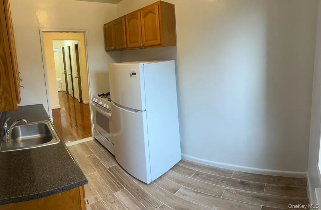 Kitchen featuring brown cabinets, wood finish floors, white appliances, and dark countertops Kitchen featuring brown cabinets, wood finish floors, white appliances, and dark countertops