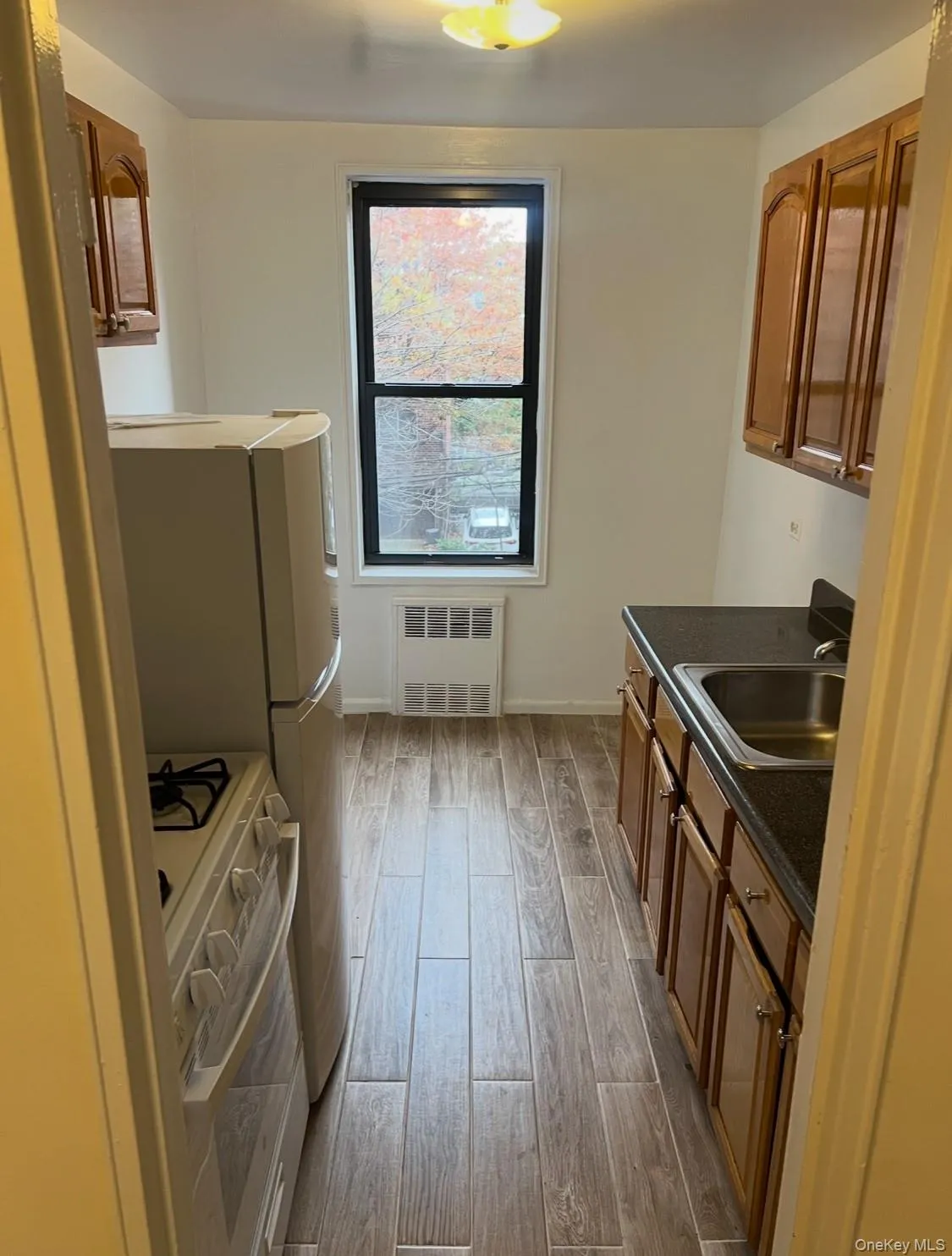 Kitchen with white range with gas cooktop, wood finish floors, brown cabinets, and radiator Kitchen with white range with gas cooktop, wood finish floors, brown cabinets, and radiator