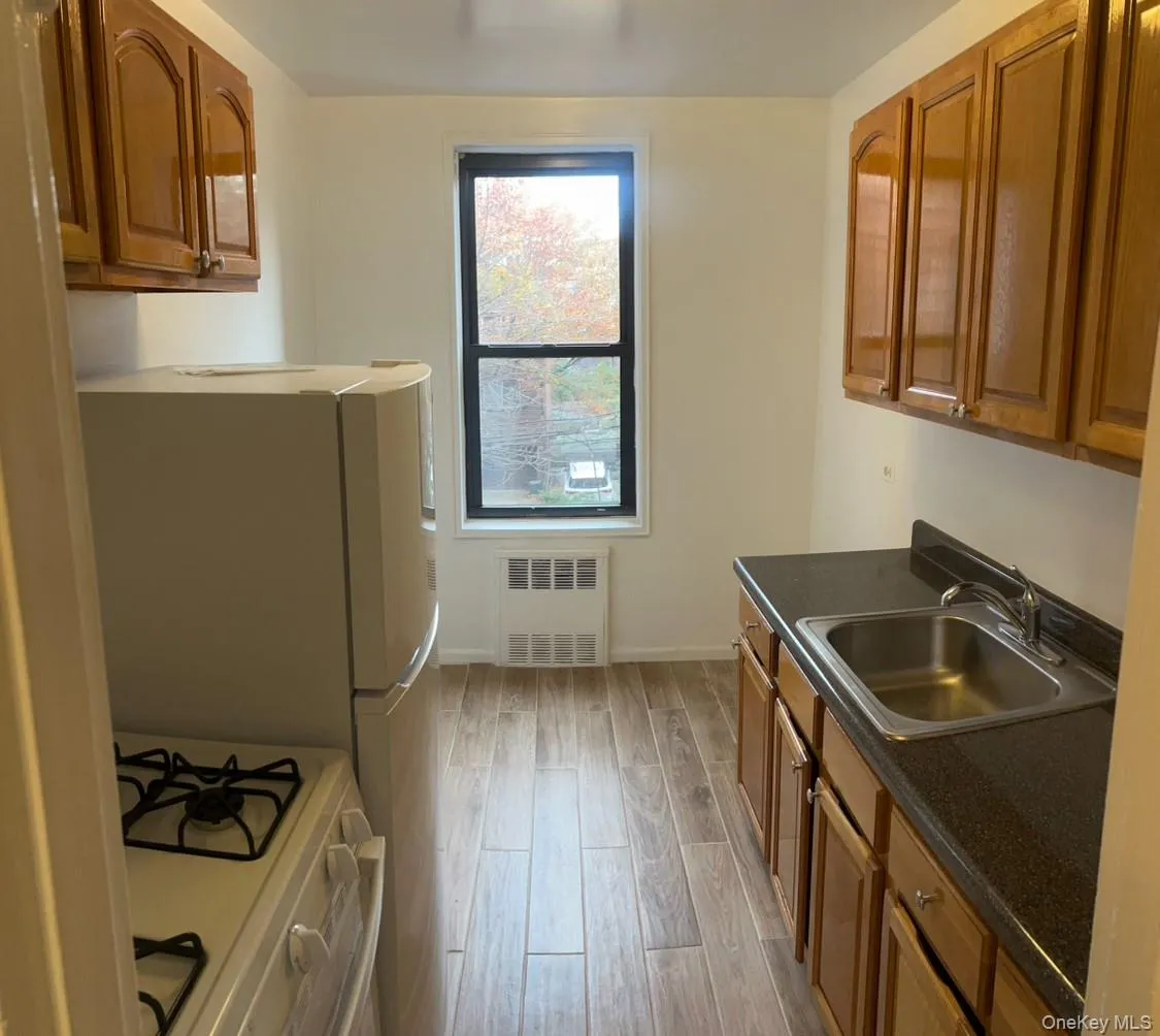 Kitchen featuring brown cabinets, white range with gas stovetop, light wood-style flooring, radiator, and dark stone countertops Kitchen featuring brown cabinets, white range with gas stovetop, light wood-style flooring, radiator, and dark stone countertops