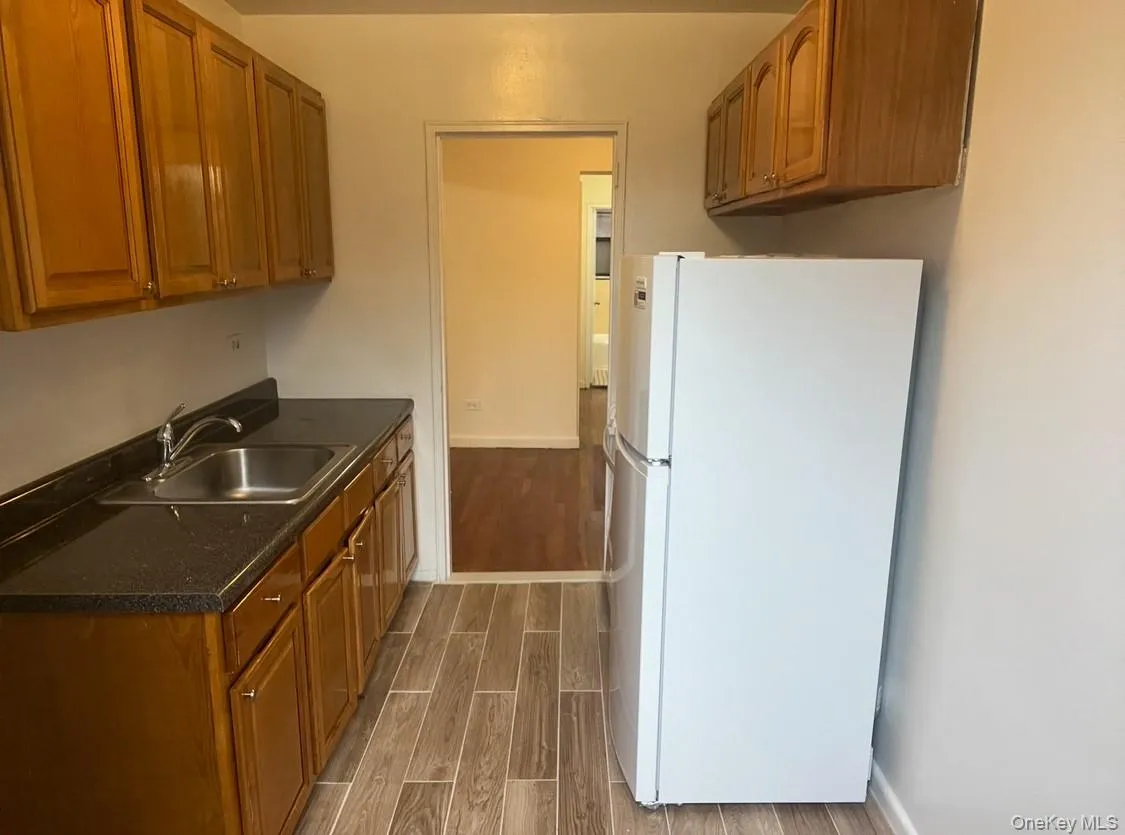 Kitchen with freestanding refrigerator, wood tiled floors, and brown cabinetry Kitchen with freestanding refrigerator, wood tiled floors, and brown cabinetry