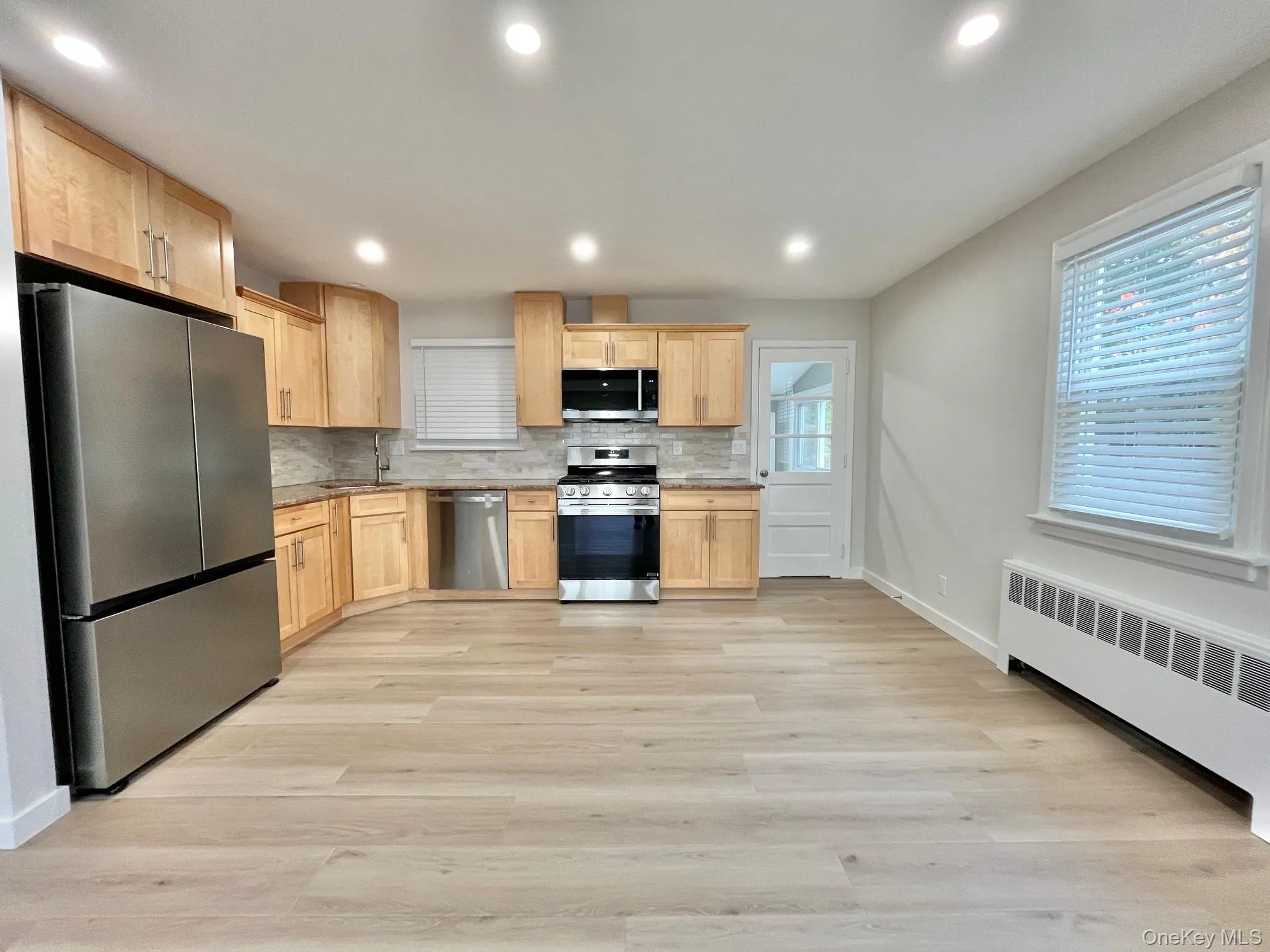 Kitchen with light brown cabinetry, stainless steel appliances, decorative backsplash, light wood-type flooring, and recessed lighting Kitchen with light brown cabinetry, stainless steel appliances, decorative backsplash, light wood-type flooring, and recessed lighting