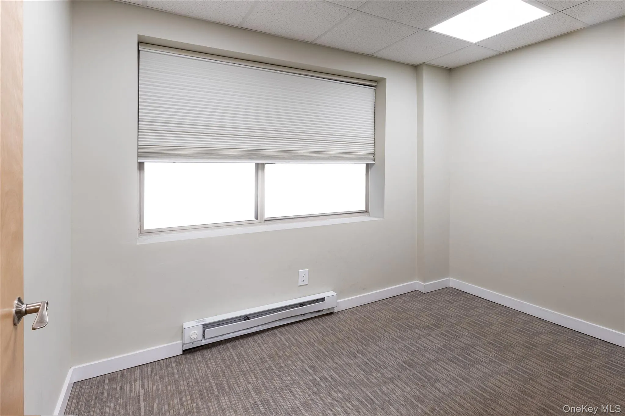 Empty room featuring dark colored carpet, a baseboard radiator, and a drop ceiling Empty room featuring dark colored carpet, a baseboard radiator, and a drop ceiling