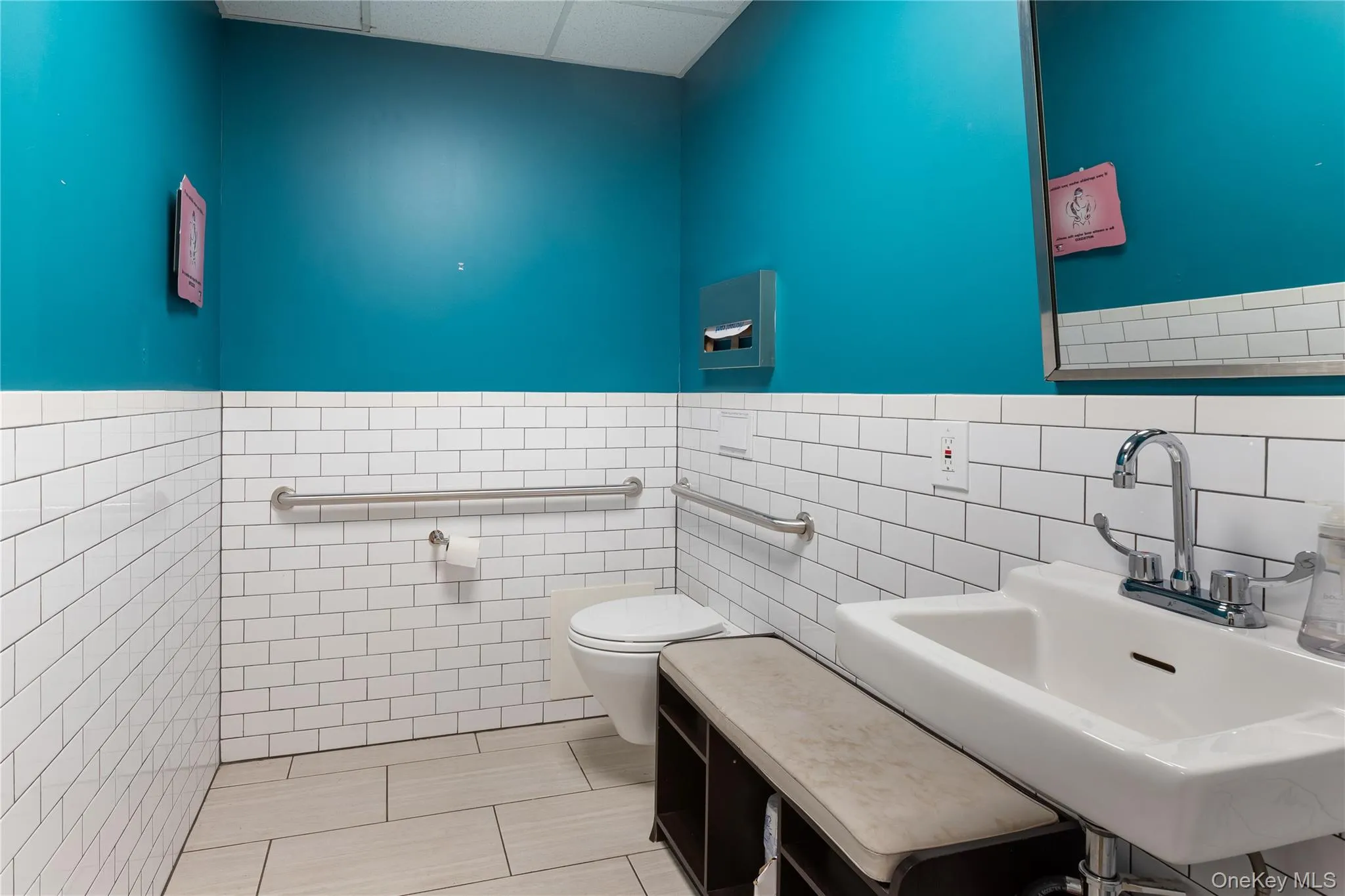 Half bath featuring light tile patterned floors, tile walls, a drop ceiling, and wainscoting Half bath featuring light tile patterned floors, tile walls, a drop ceiling, and wainscoting