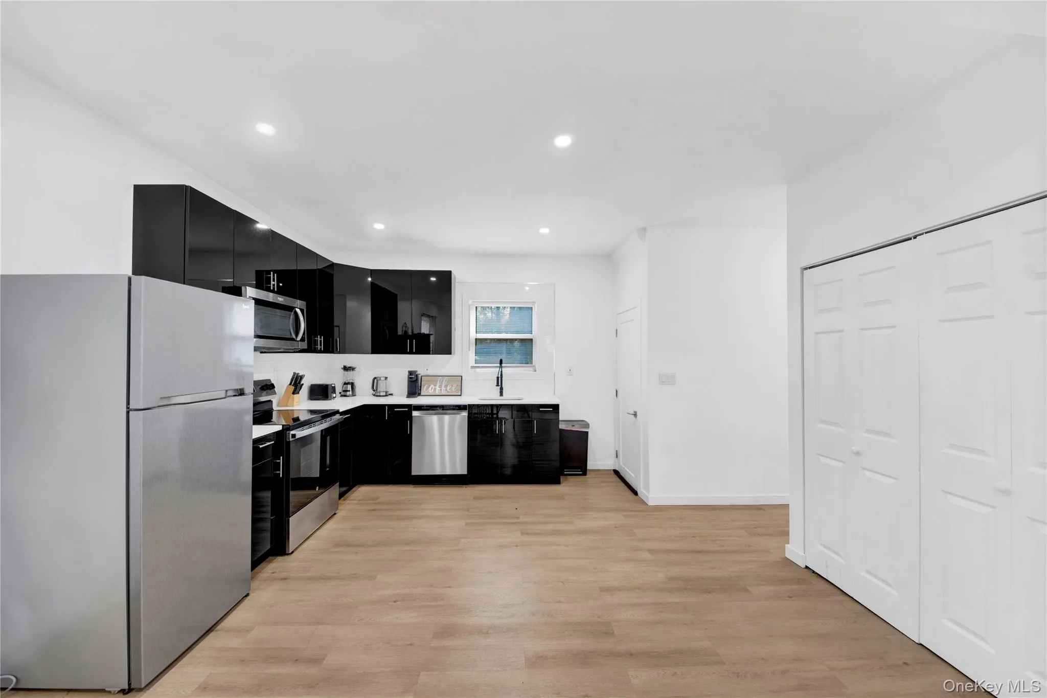 Kitchen featuring dark cabinets, appliances with stainless steel finishes, light countertops, light wood finished floors, and recessed lighting Kitchen featuring dark cabinets, appliances with stainless steel finishes, light countertops, light wood finished floors, and recessed lighting