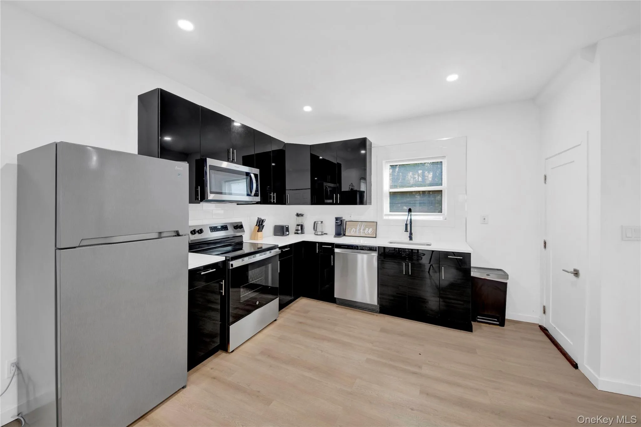 Kitchen with dark cabinetry, stainless steel appliances, light wood-type flooring, recessed lighting, and modern cabinets Kitchen with dark cabinetry, stainless steel appliances, light wood-type flooring, recessed lighting, and modern cabinets