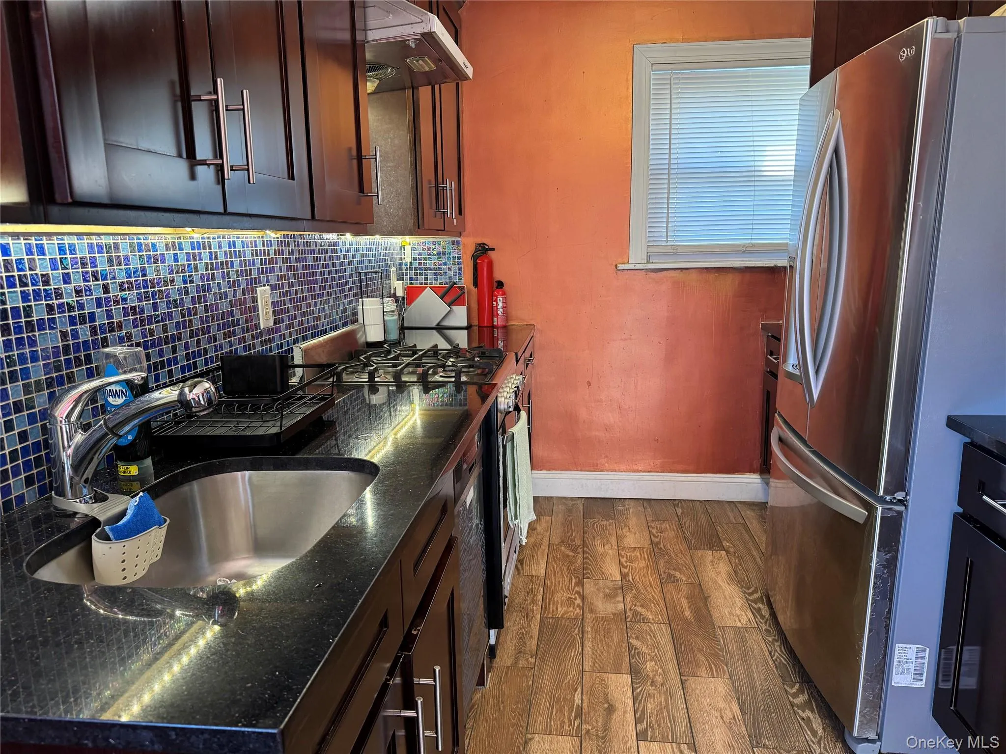Kitchen with freestanding refrigerator, dark wood-style flooring, under cabinet range hood, backsplash, and gas range Kitchen with freestanding refrigerator, dark wood-style flooring, under cabinet range hood, backsplash, and gas range