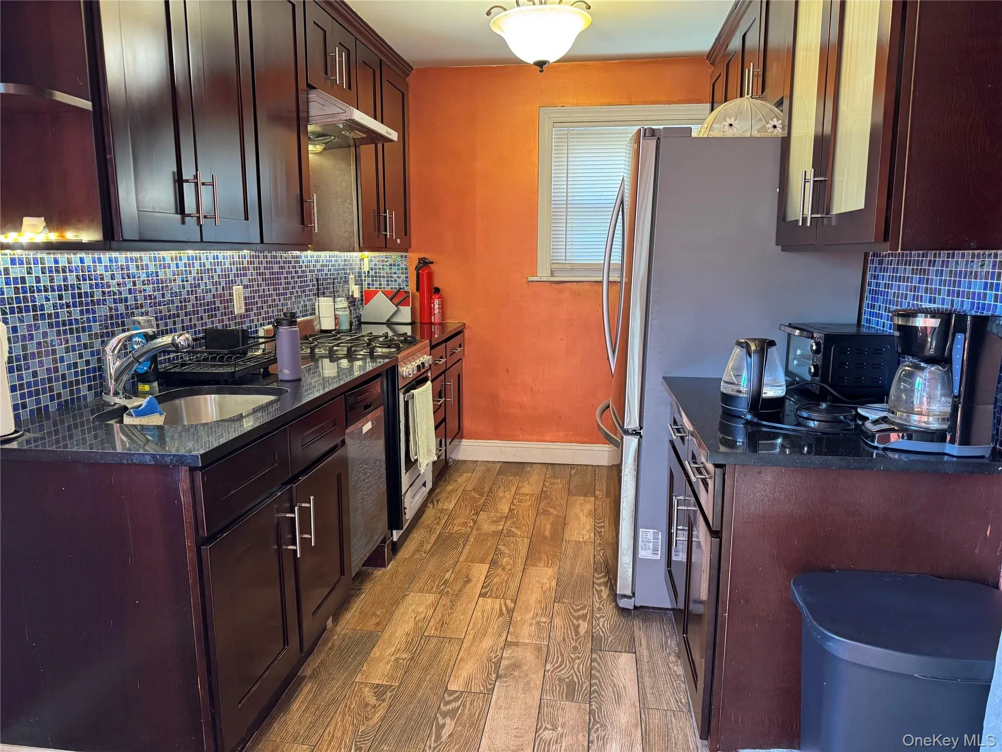Kitchen with tasteful backsplash, open shelves, dark wood-type flooring, dark stone counters, and dark brown cabinets Kitchen with tasteful backsplash, open shelves, dark wood-type flooring, dark stone counters, and dark brown cabinets