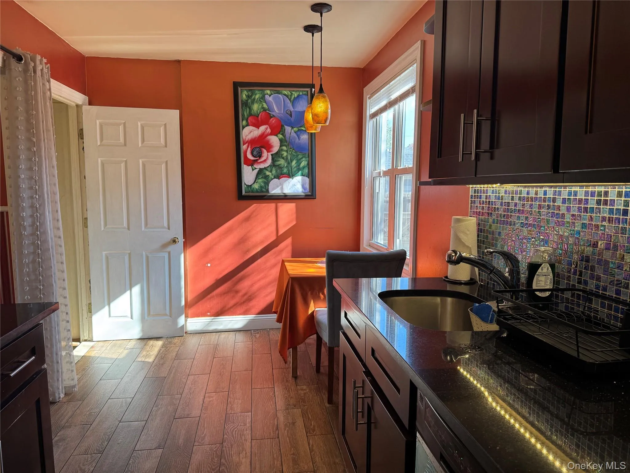 Kitchen with decorative light fixtures, dark wood-style floors, backsplash, dark stone countertops, and dark brown cabinetry Kitchen with decorative light fixtures, dark wood-style floors, backsplash, dark stone countertops, and dark brown cabinetry