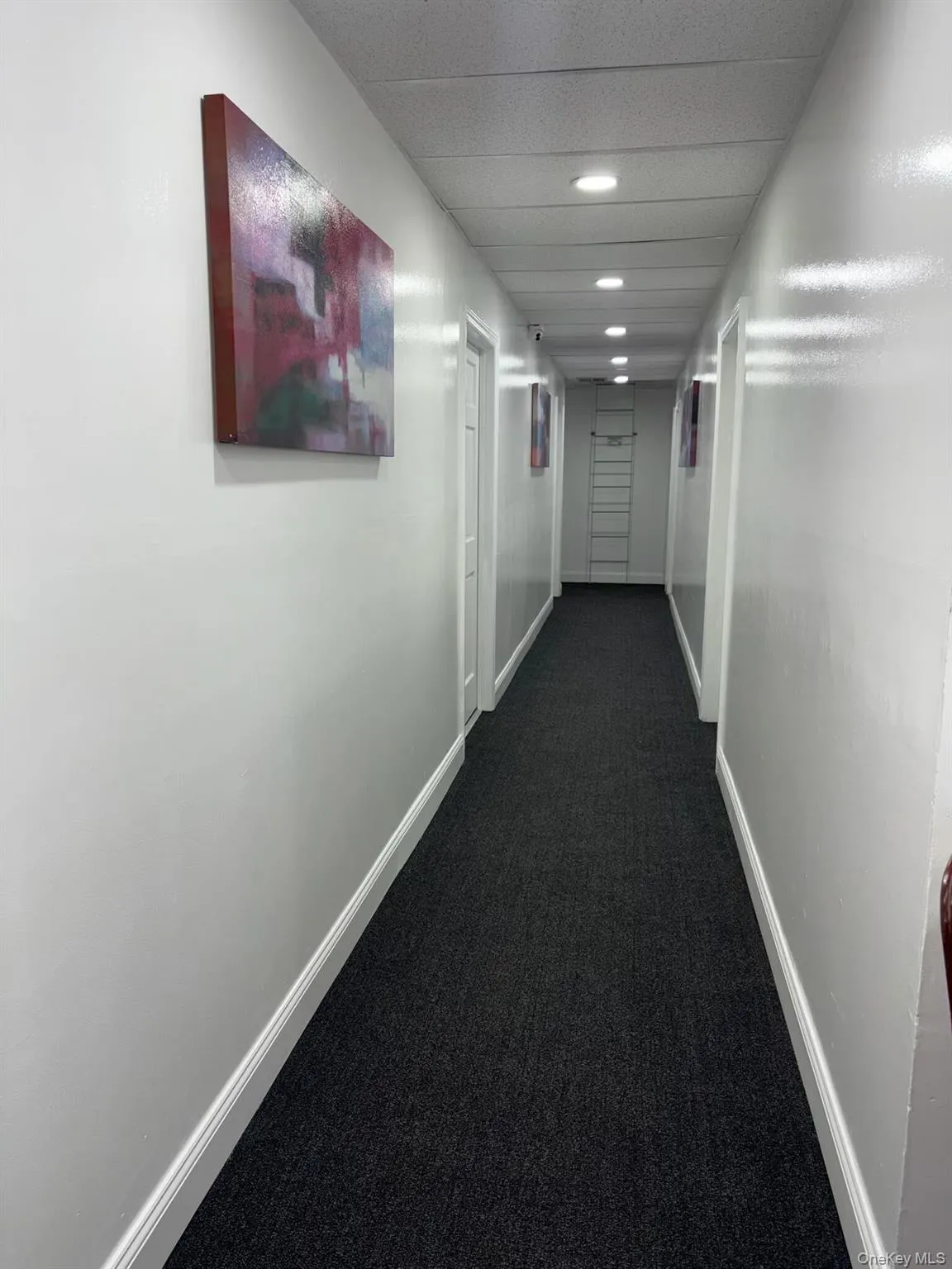 Hall featuring dark colored carpet and baseboards Hall featuring dark colored carpet and baseboards