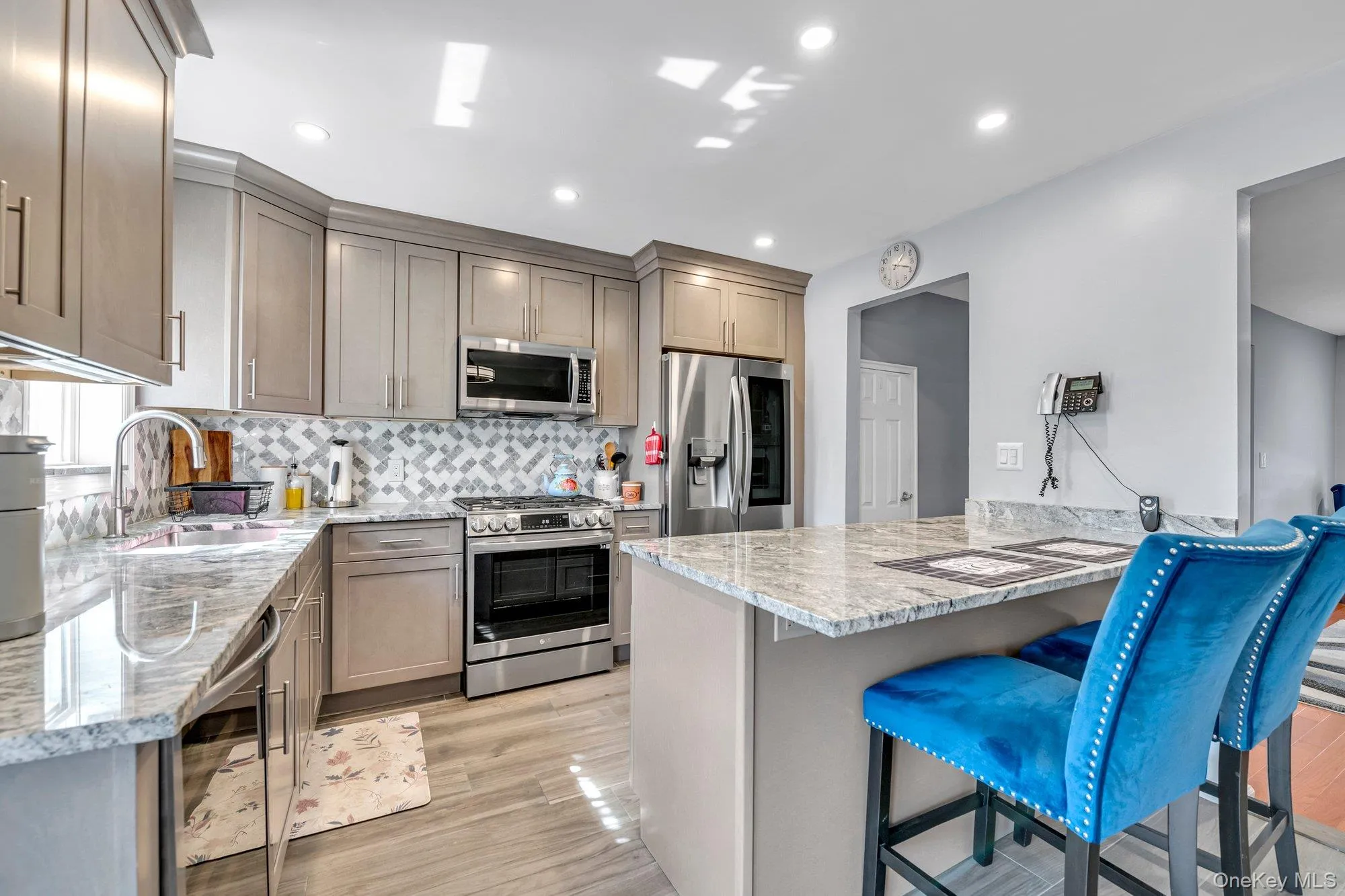 Kitchen with light stone counters, a breakfast bar, appliances with stainless steel finishes, decorative backsplash, and wine cooler Kitchen with light stone counters, a breakfast bar, appliances with stainless steel finishes, decorative backsplash, and wine cooler