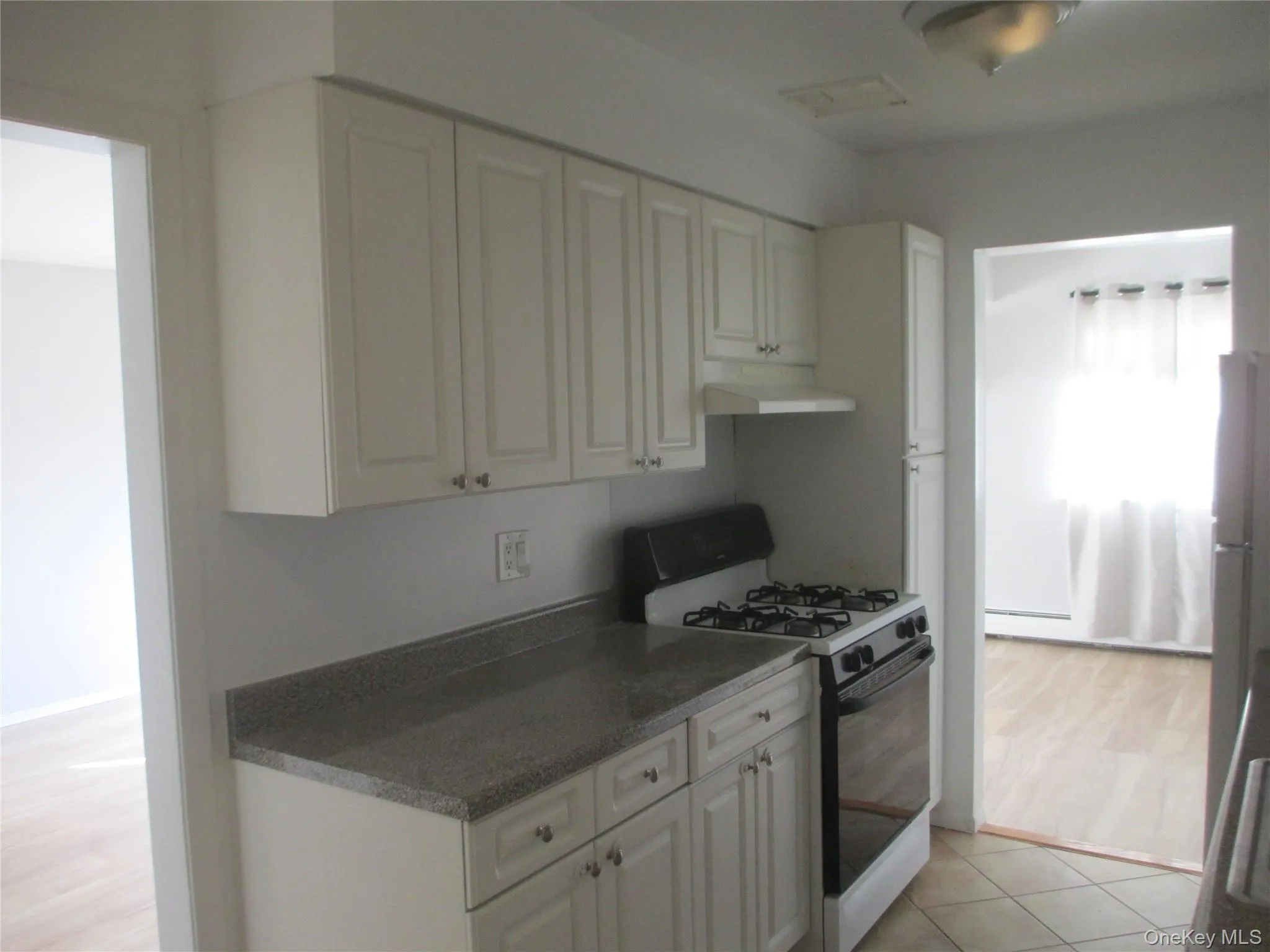 Kitchen featuring gas range oven, white cabinets, dark countertops, and under cabinet range hood Kitchen featuring gas range oven, white cabinets, dark countertops, and under cabinet range hood