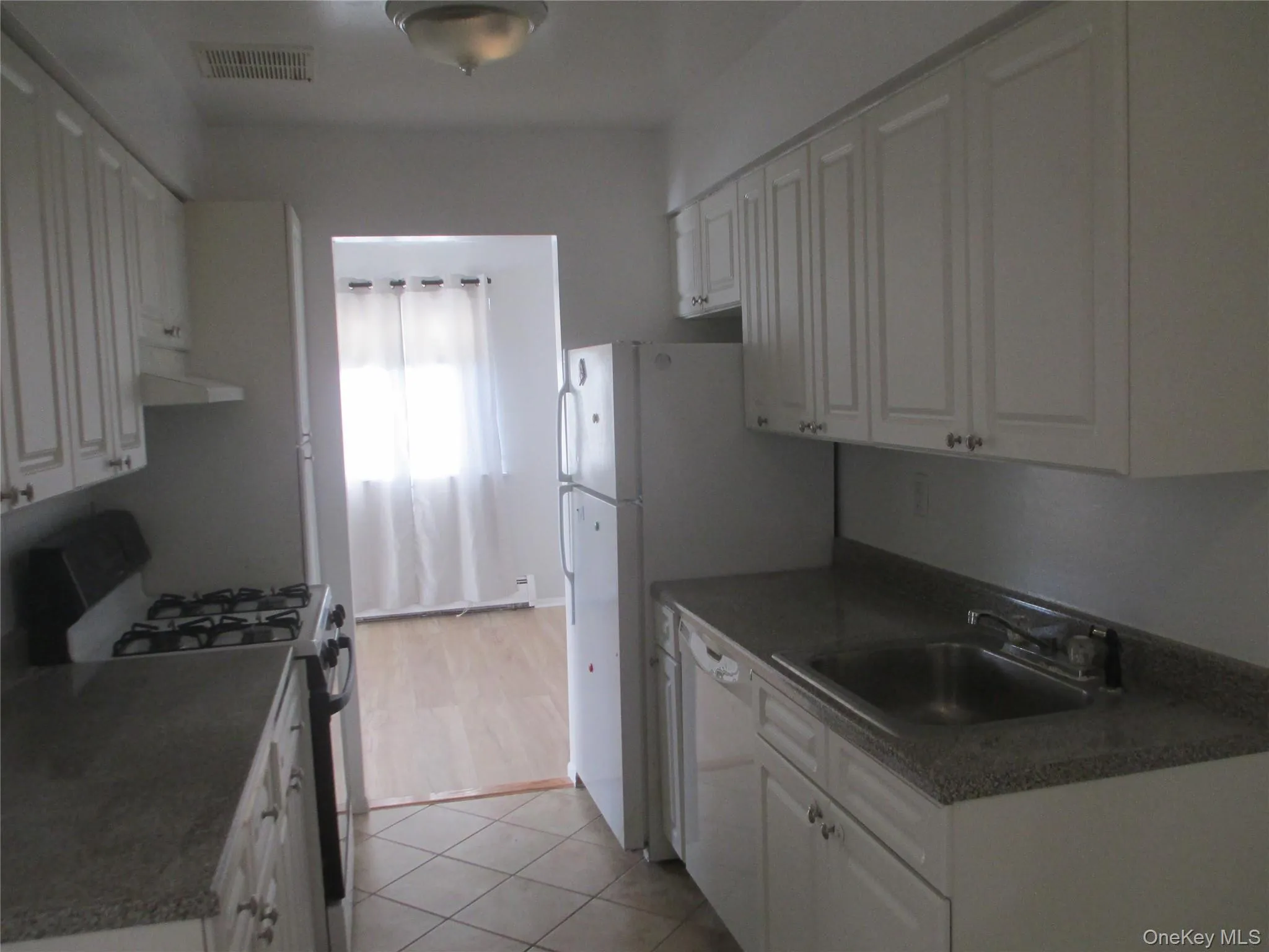 Kitchen featuring white appliances, white cabinets, dark countertops, extractor fan, and light tile patterned floors Kitchen featuring white appliances, white cabinets, dark countertops, extractor fan, and light tile patterned floors