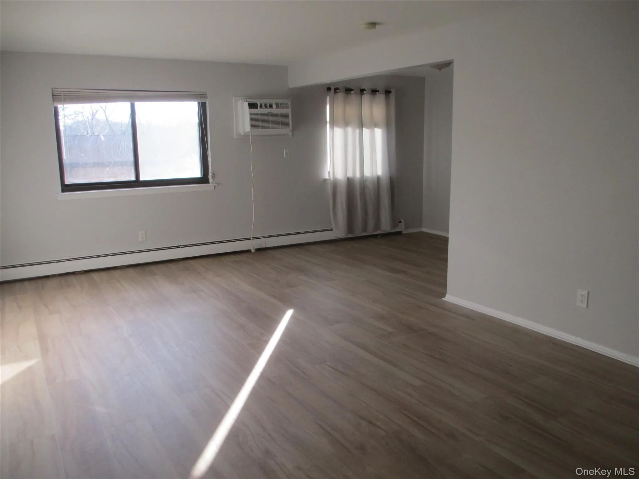 Unfurnished room with a baseboard heating unit, wood finished floors, and a wall mounted air conditioner Unfurnished room with a baseboard heating unit, wood finished floors, and a wall mounted air conditioner
