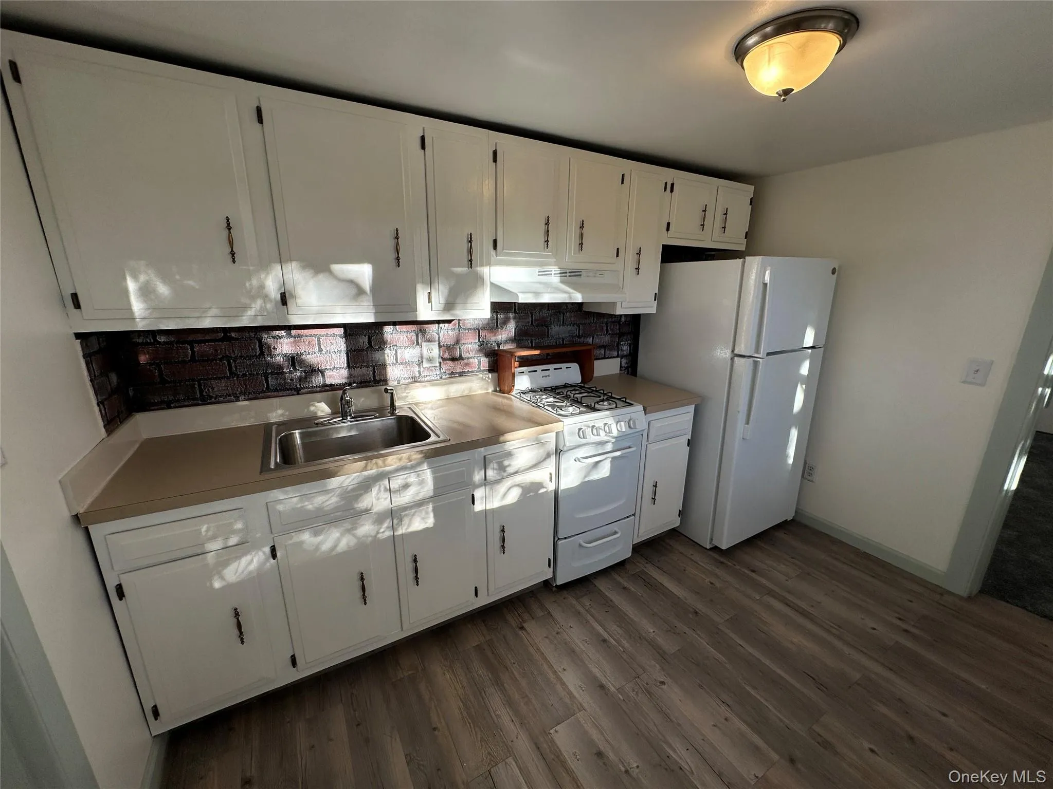 Kitchen featuring white cabinetry, white appliances, tasteful backsplash, dark wood finished floors, and light countertops Kitchen featuring white cabinetry, white appliances, tasteful backsplash, dark wood finished floors, and light countertops