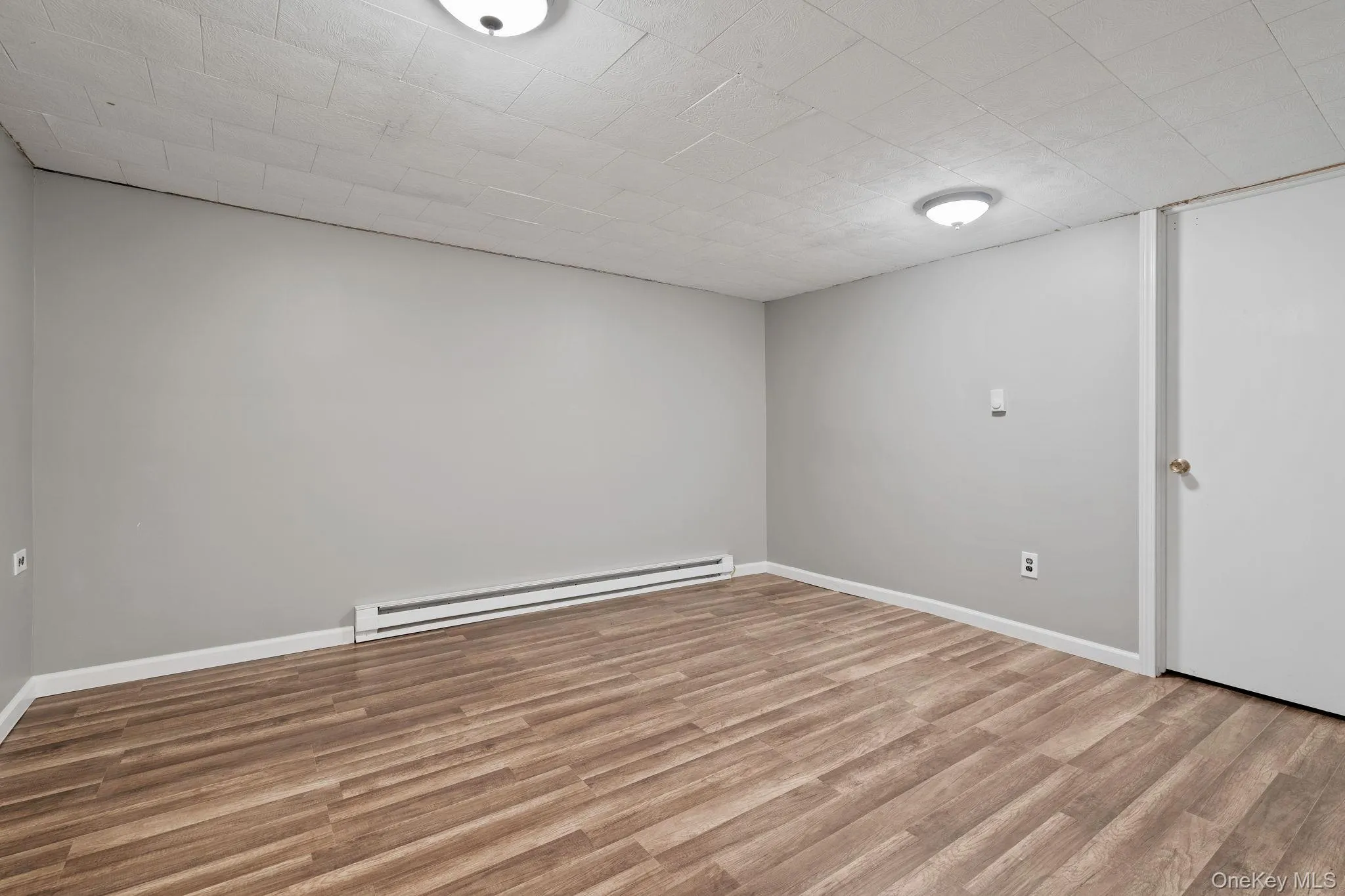 Finished below grade area with light wood-style flooring and baseboard heating Finished below grade area with light wood-style flooring and baseboard heating