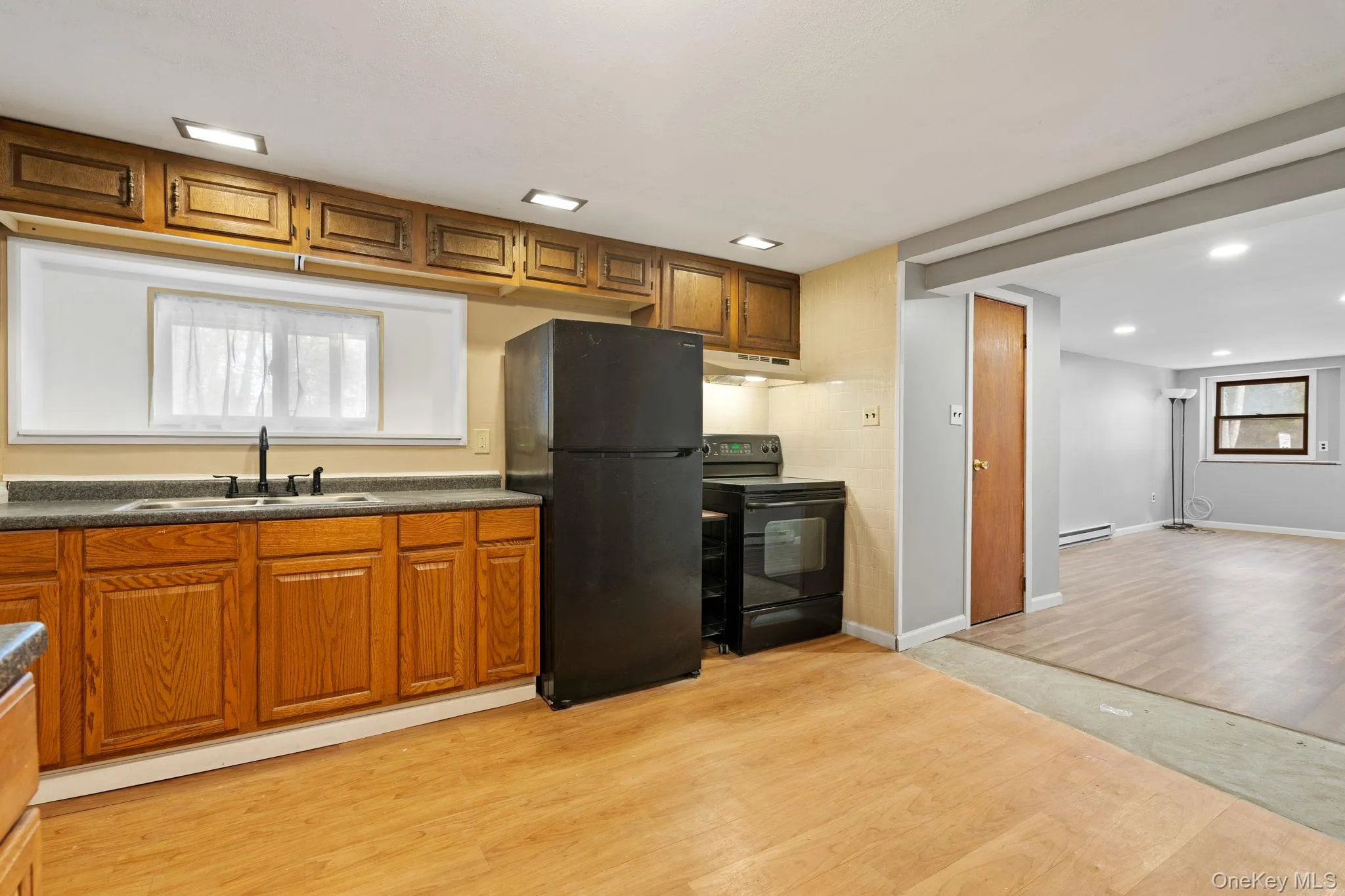 Kitchen featuring light wood-type flooring, black appliances, brown cabinetry, dark countertops, and recessed lighting Kitchen featuring light wood-type flooring, black appliances, brown cabinetry, dark countertops, and recessed lighting
