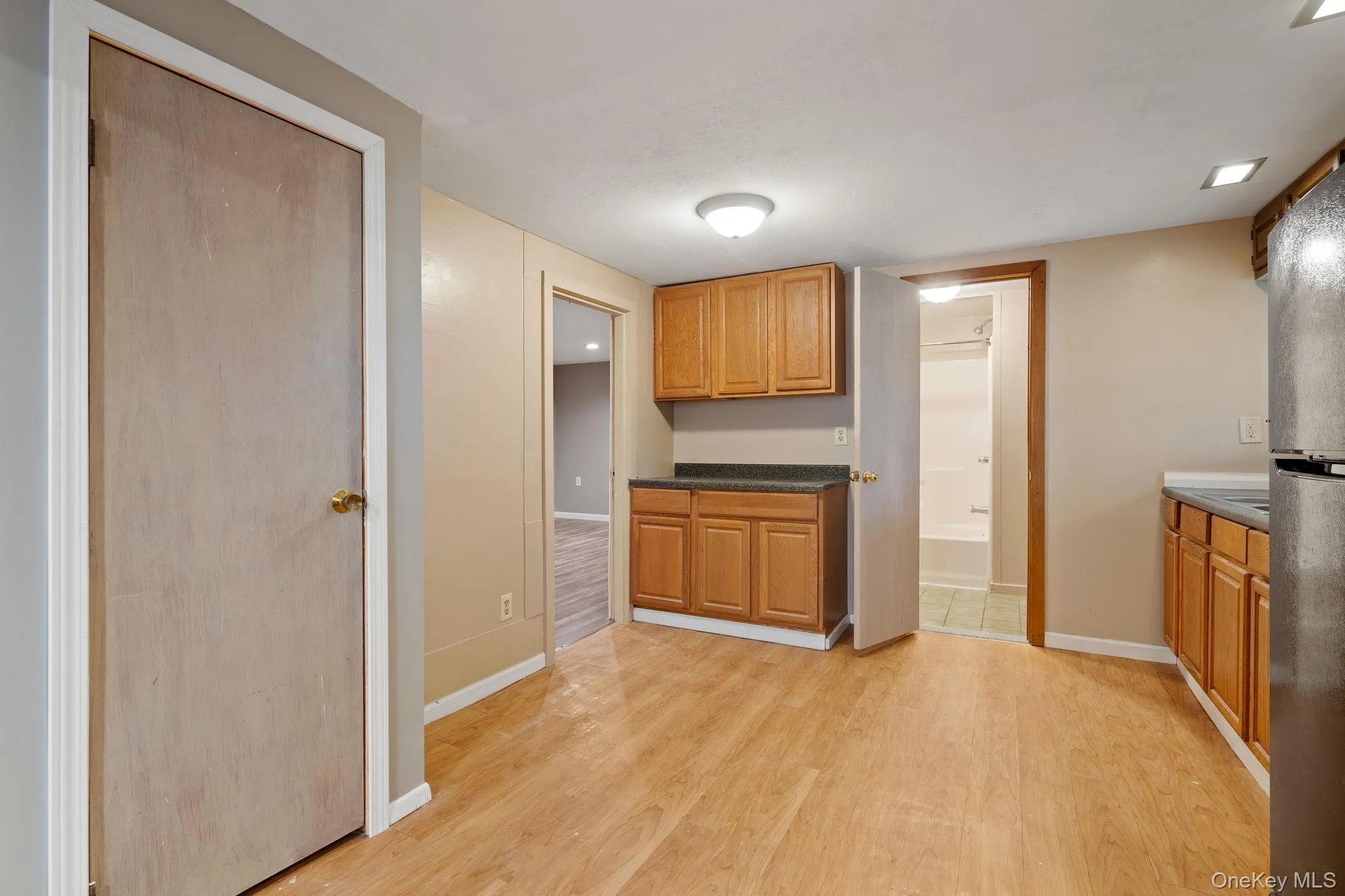 Kitchen featuring light wood-type flooring, freestanding refrigerator, dark countertops, and brown cabinets Kitchen featuring light wood-type flooring, freestanding refrigerator, dark countertops, and brown cabinets