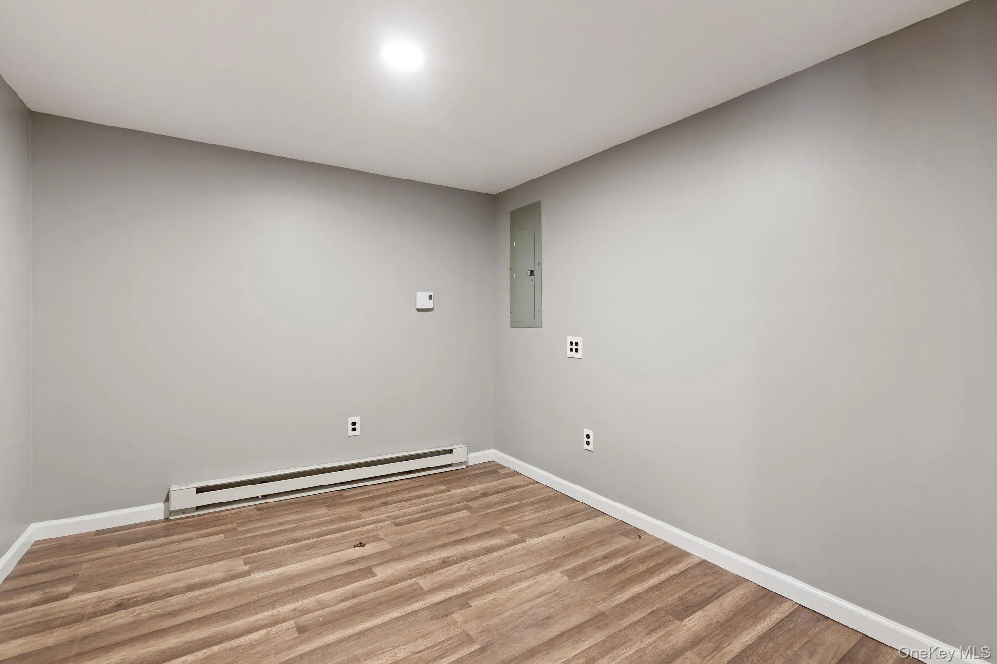 Washroom featuring a baseboard heating unit, light wood-style flooring, and electric panel Washroom featuring a baseboard heating unit, light wood-style flooring, and electric panel