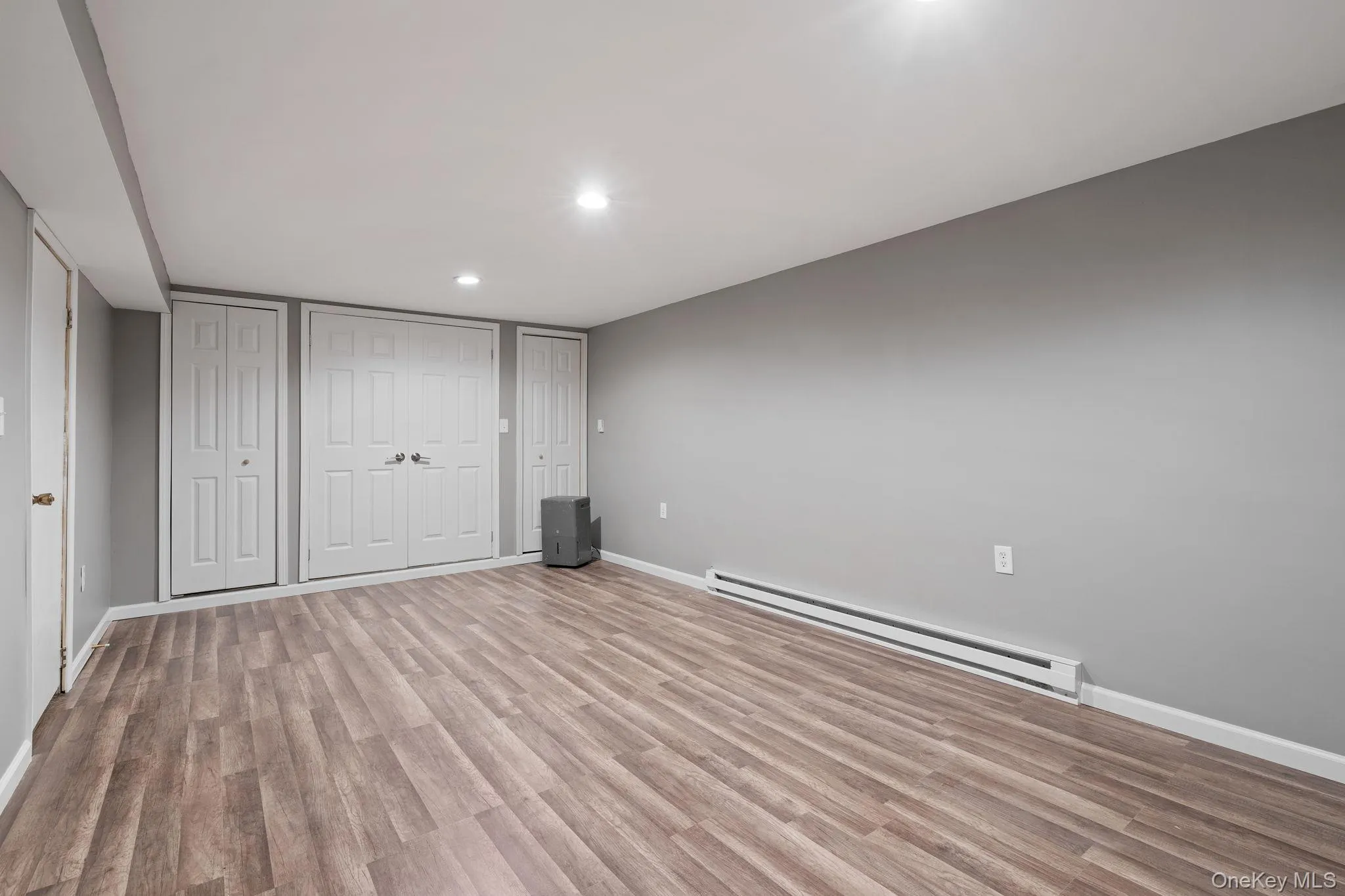 Unfurnished bedroom with a baseboard heating unit, two closets, light wood-type flooring, and recessed lighting Unfurnished bedroom with a baseboard heating unit, two closets, light wood-type flooring, and recessed lighting
